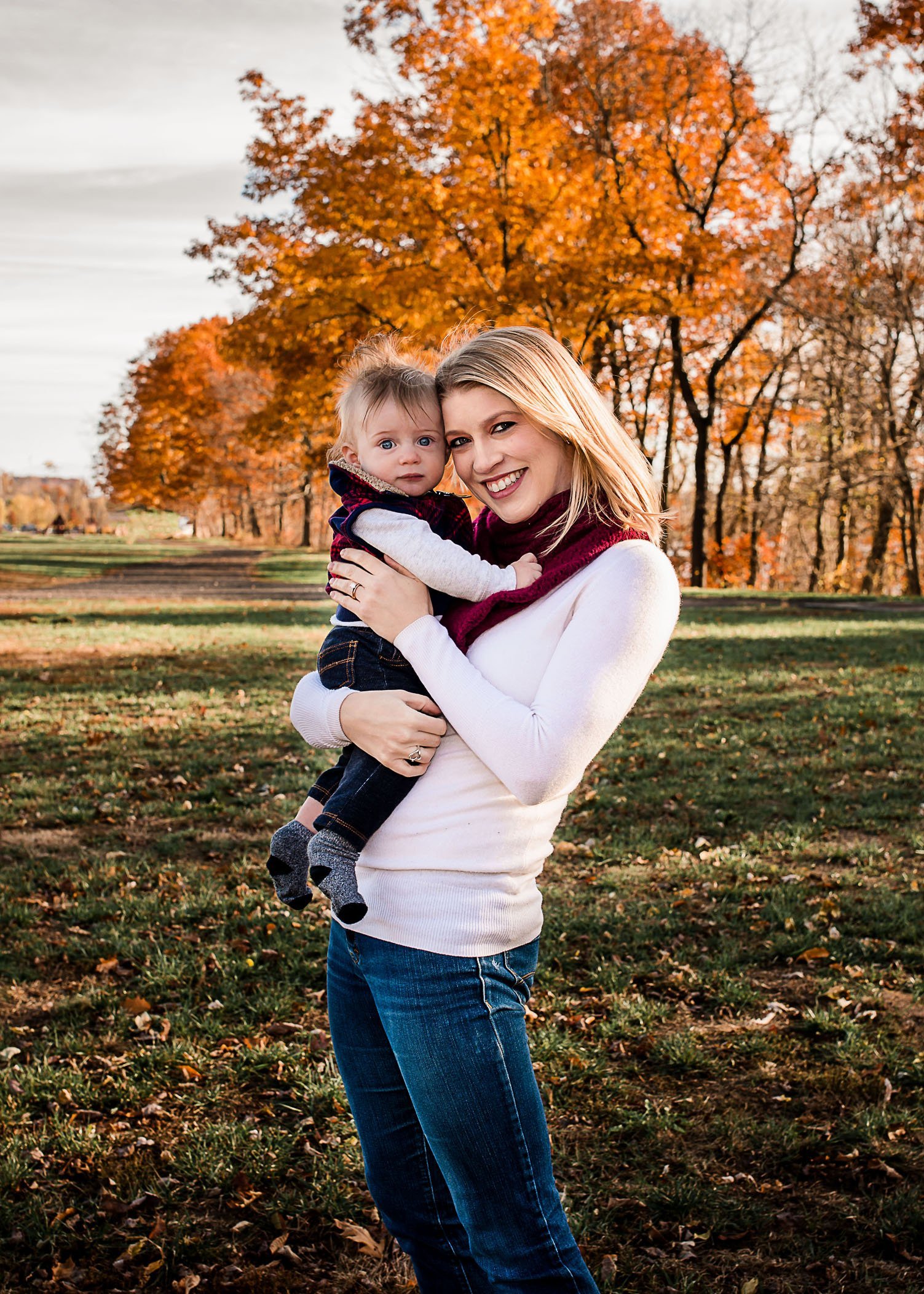 Mom holding 6 month old baby boy outside with orange fall foliage