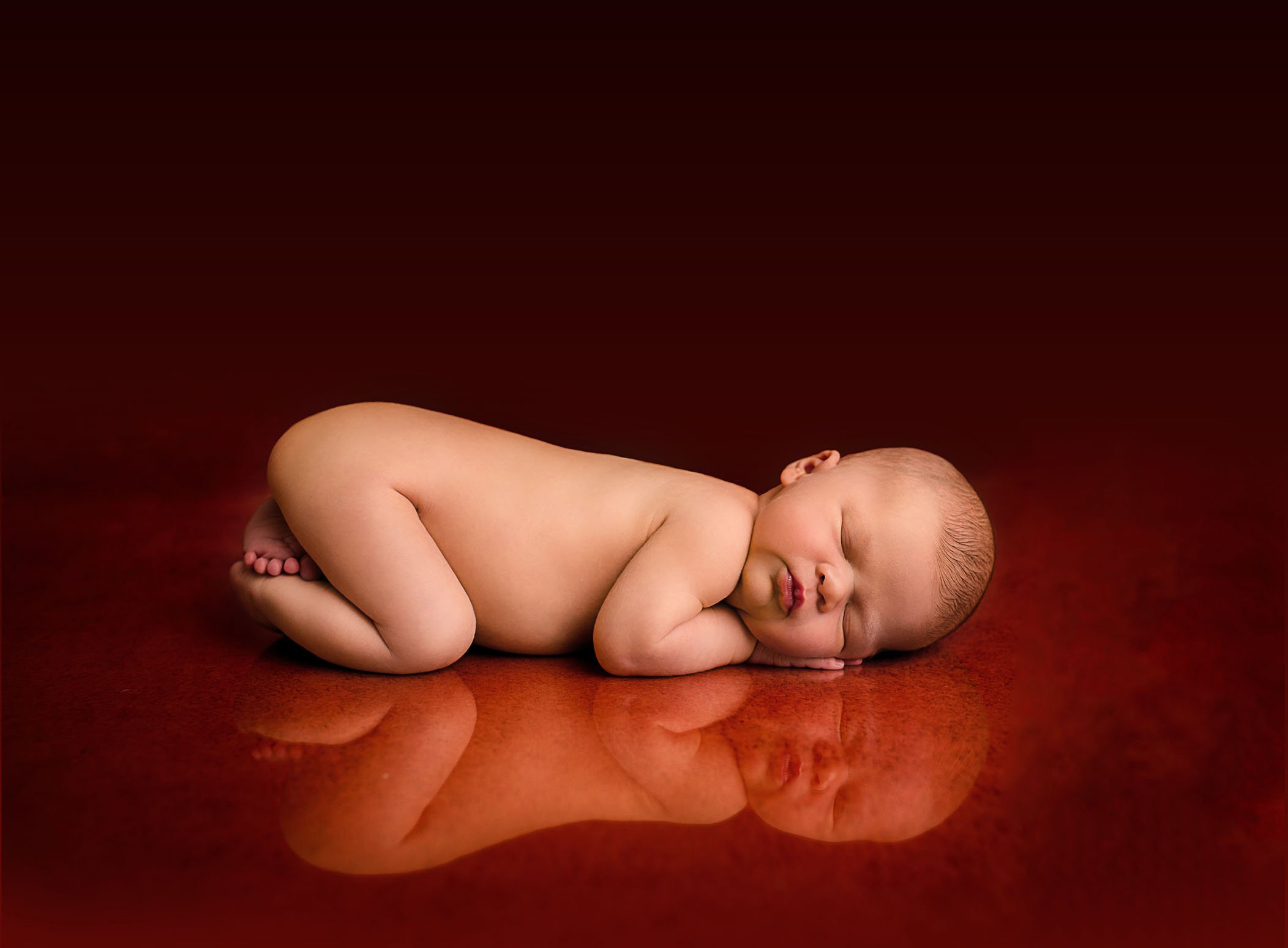 newborn baby on red background with reflection under her