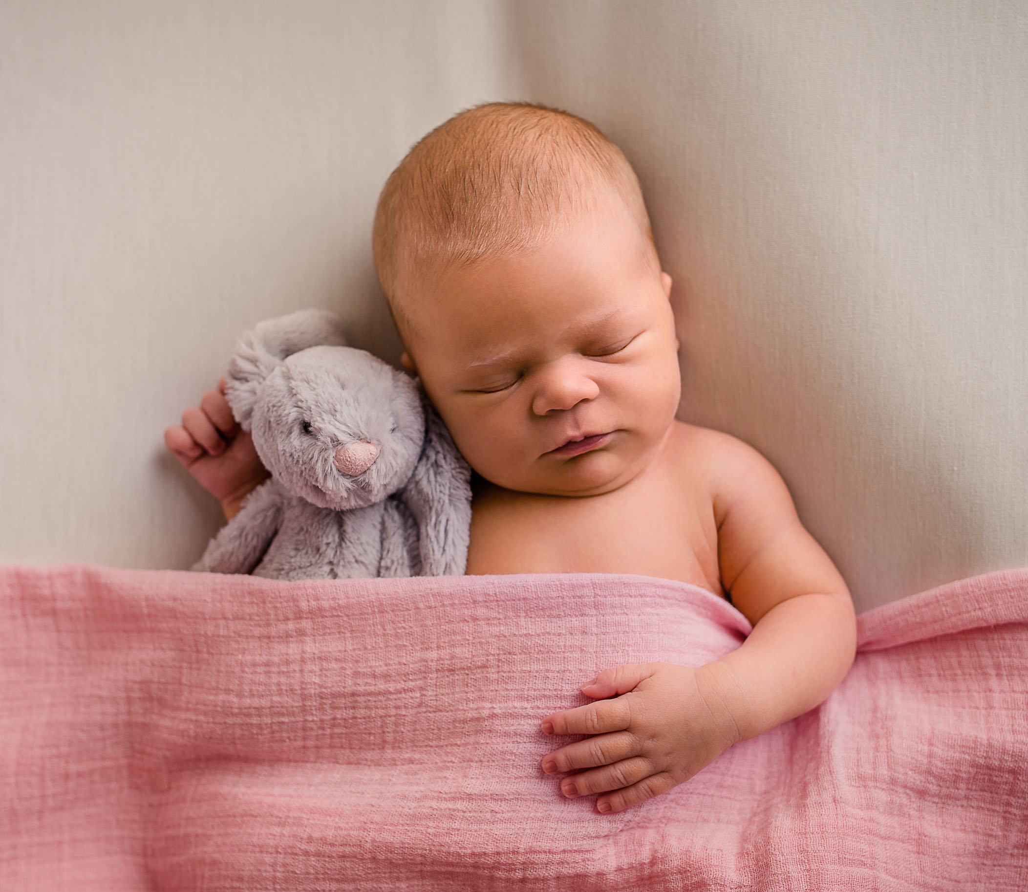 newborn baby girl sleeping under pink blanket with stuffed rabbit toy