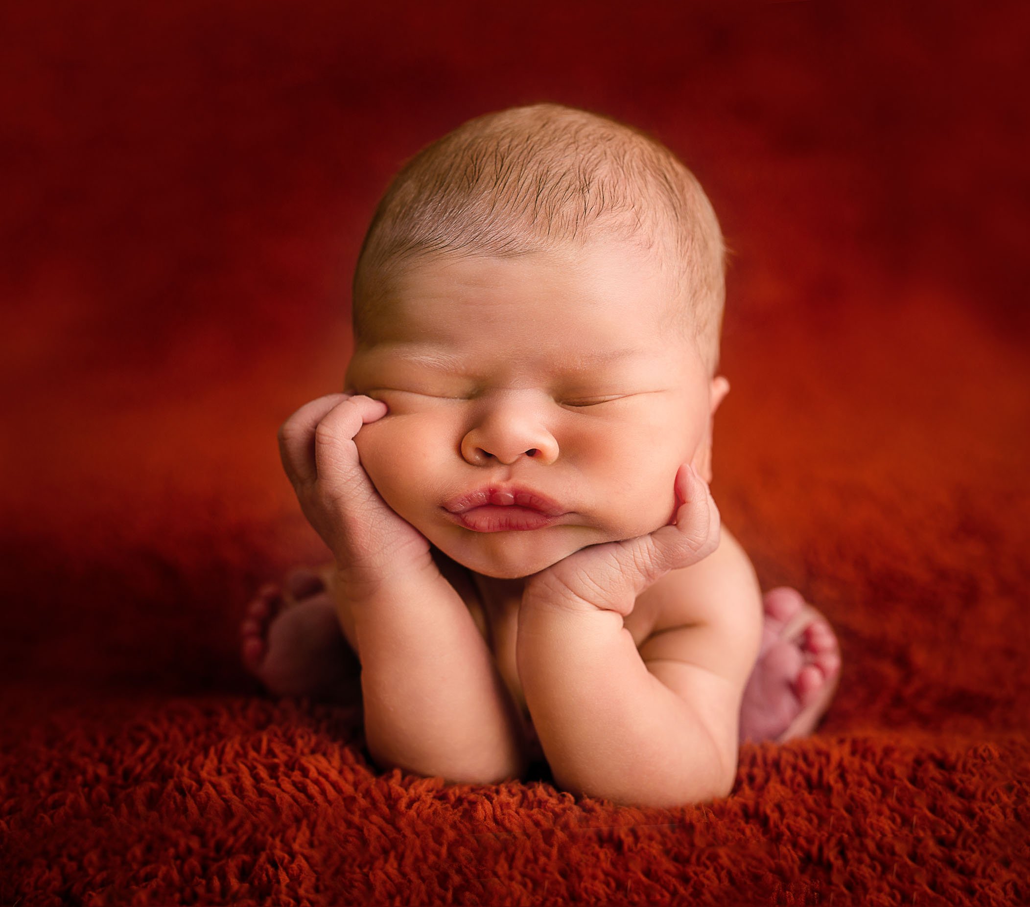 newborn baby in froggy pose with pouty lips on red background