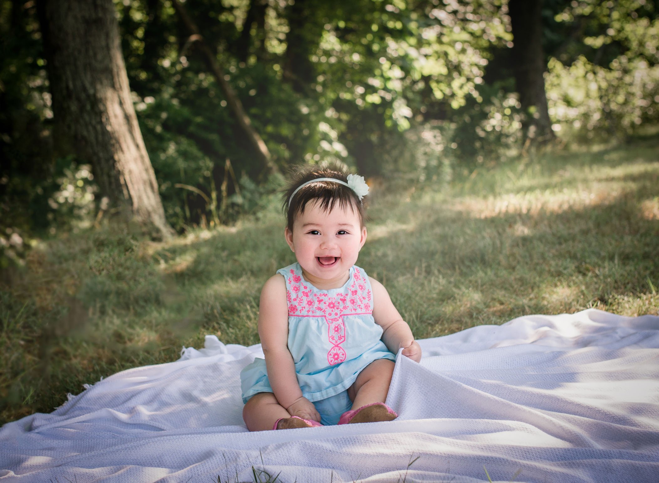 6 month old baby girl smiling outside sitting on a blanket in the grass