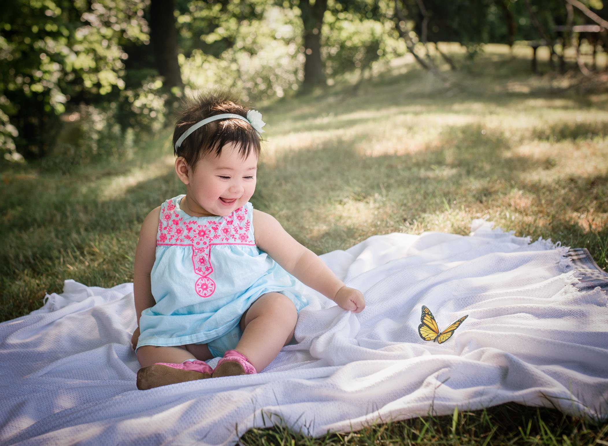 6 month old baby girl sitting on a blanket smiling at a butterfly that landed on her blanket in the sun