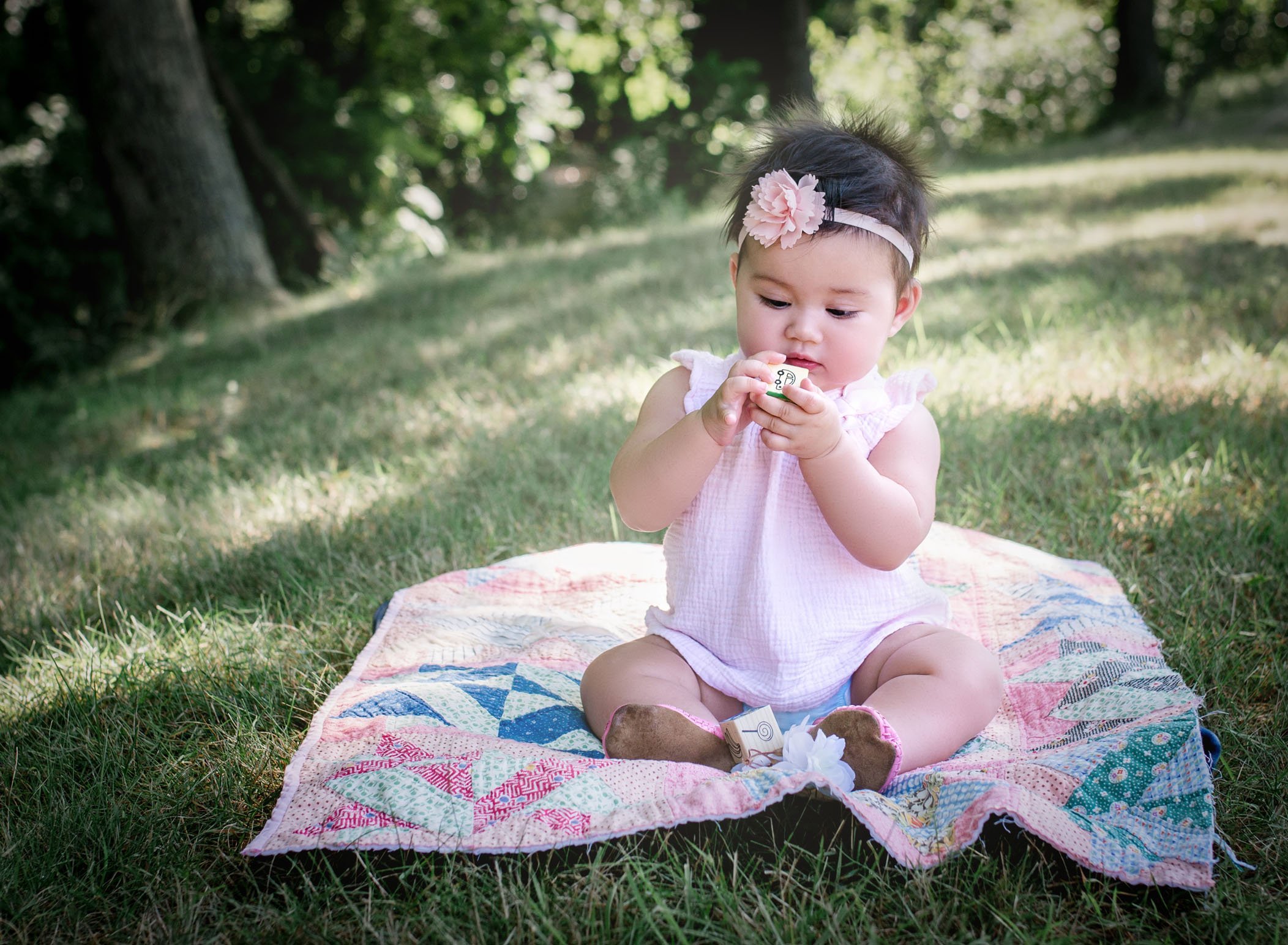 6 month old baby girl sitting on a blanket in the grass looking at a block in her hand