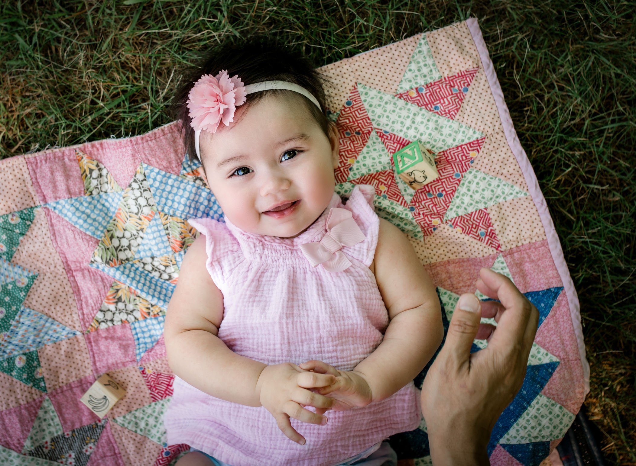 6 month old baby girl lying on her back on a pink quilt on the grass smiling