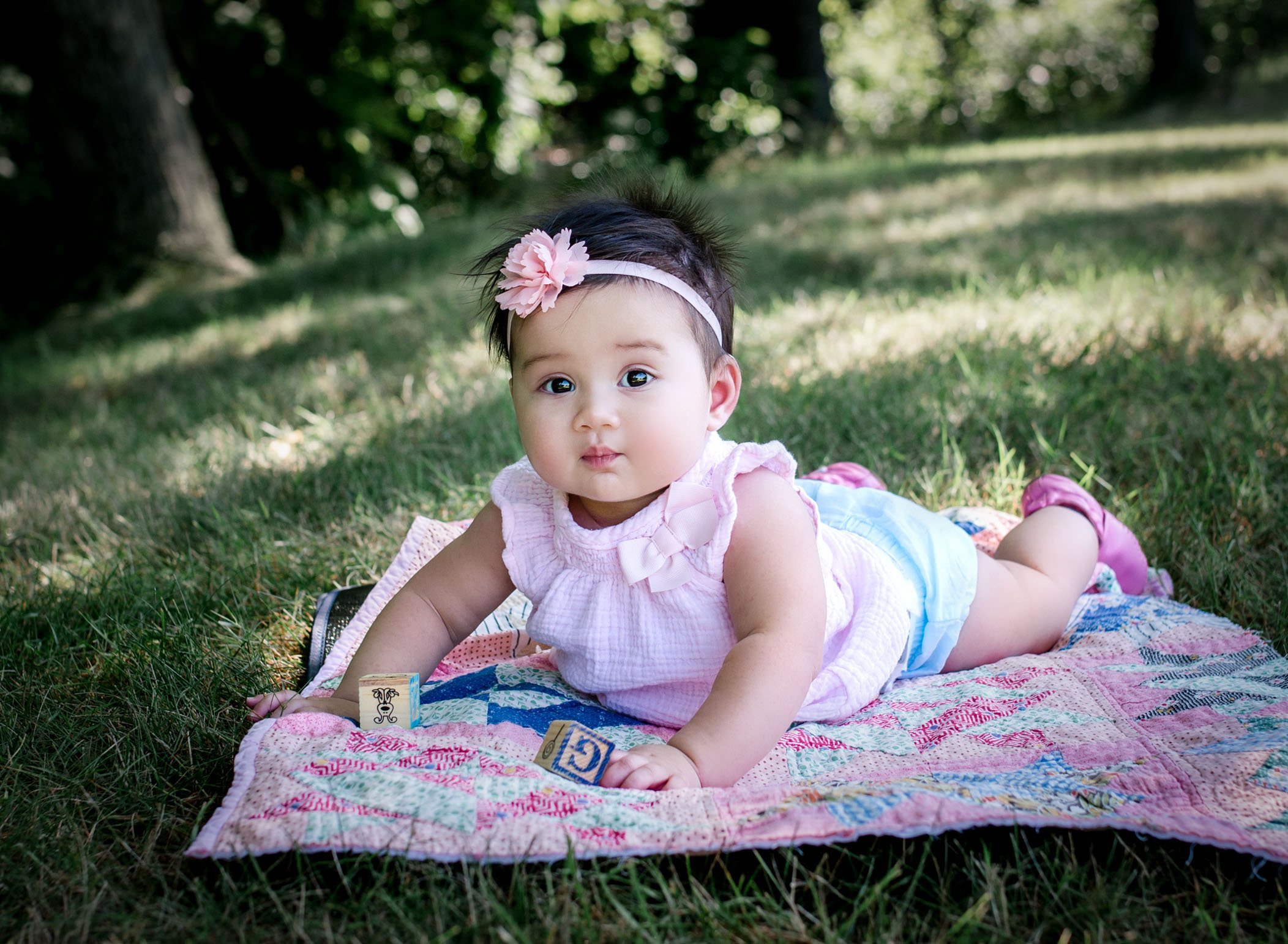 6 month old baby girl lying on her tummy on a quilt on the grass playing with blocks