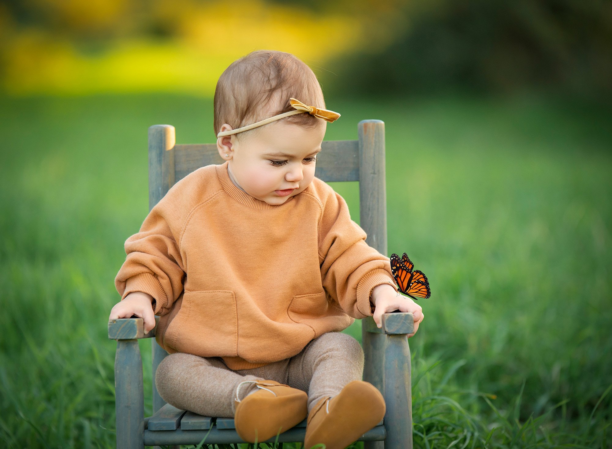 toddler girl sitting in rustic chair with orange butterfly sitting on her hand