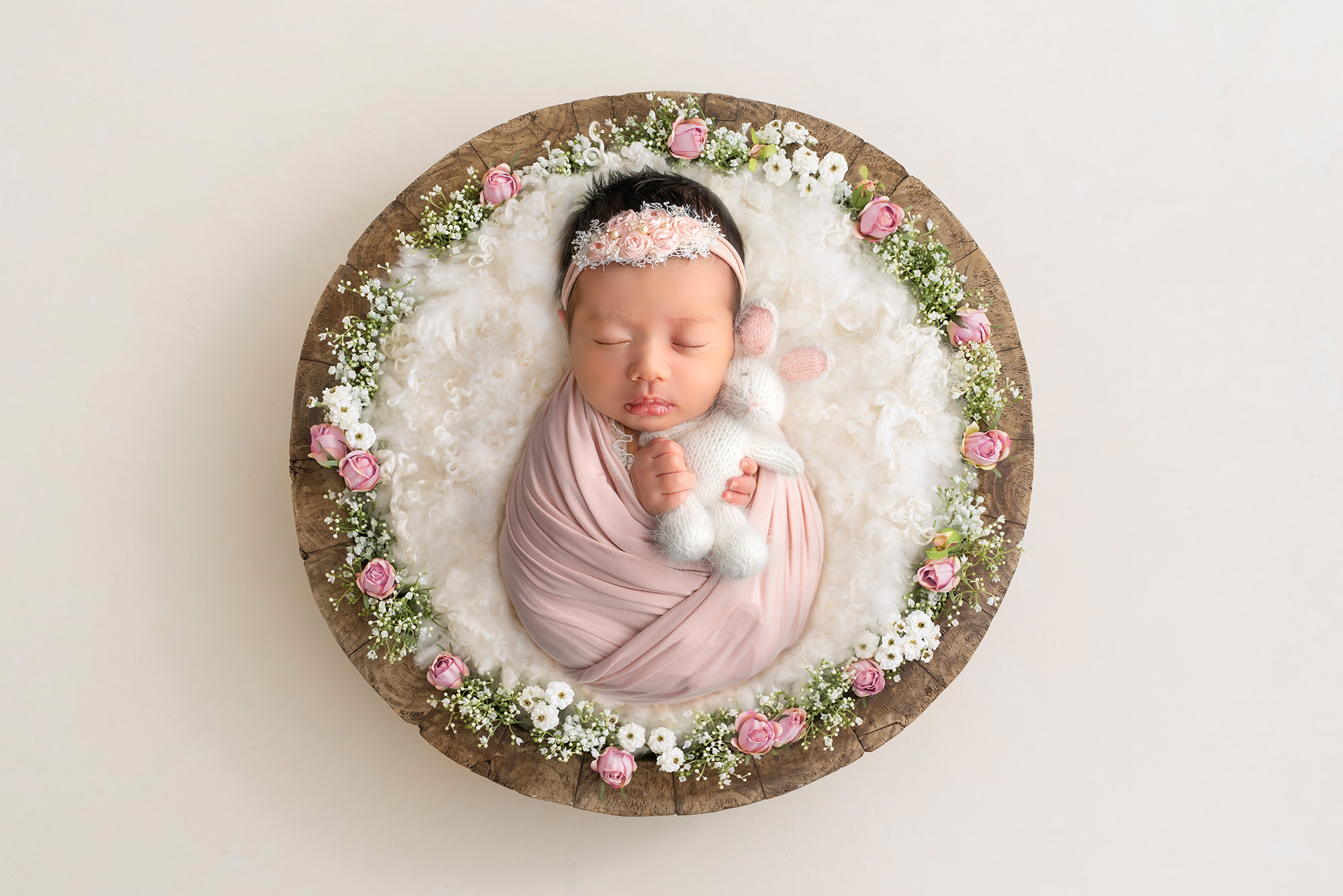 posed newborn photography session Baby Sophie cradling a white bunny amidst pink roses