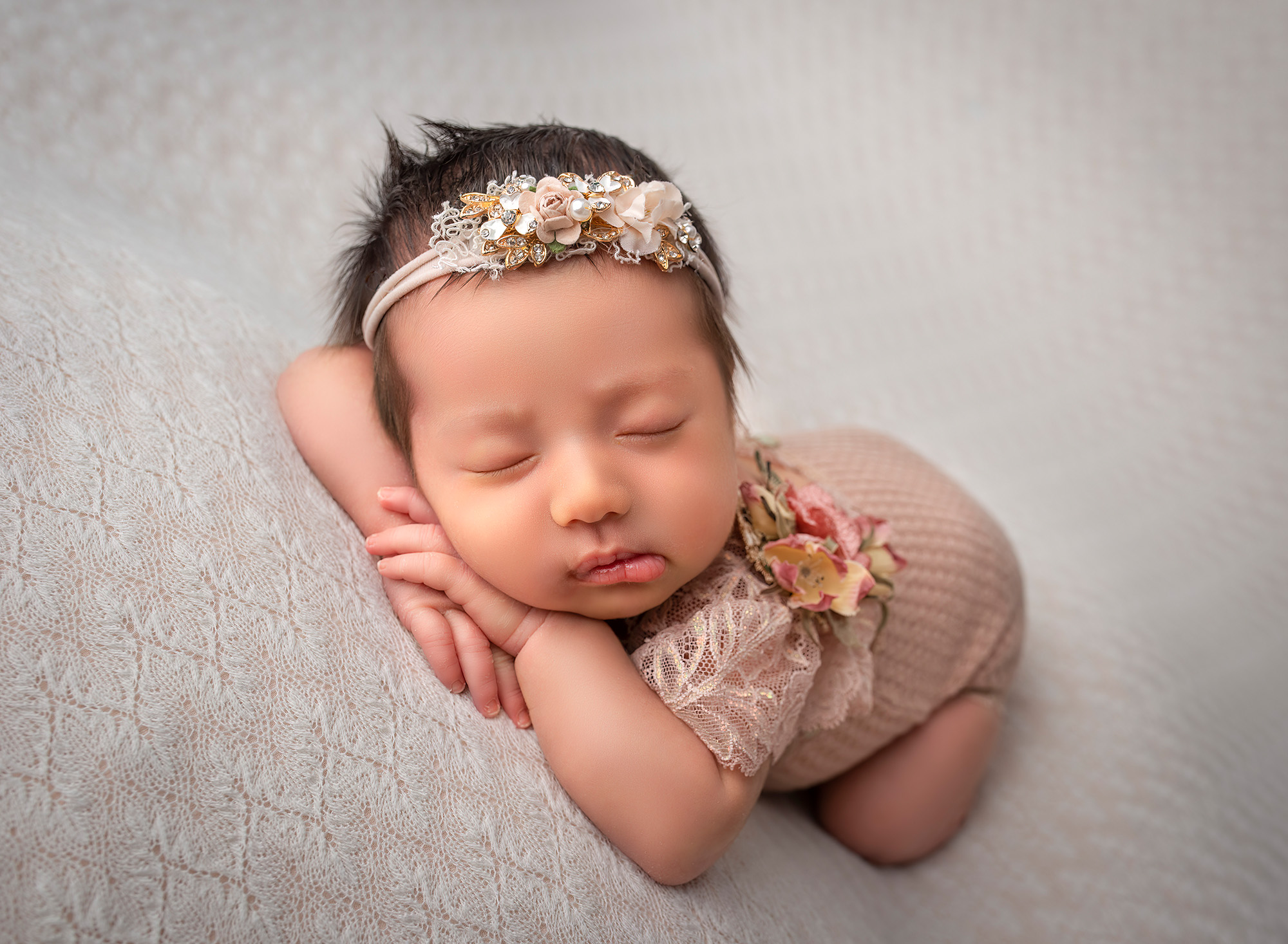 posed newborn photography session Sophie wearing a blush onesie adorned with lace and flowers.