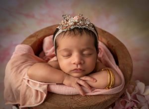 newborn baby girl asleep in honey pot draped in pink wearing gold bracelets