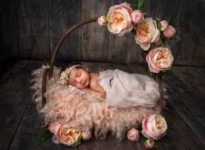 precious newborn baby girl asleep on wooden bed surrounded by pink flowers