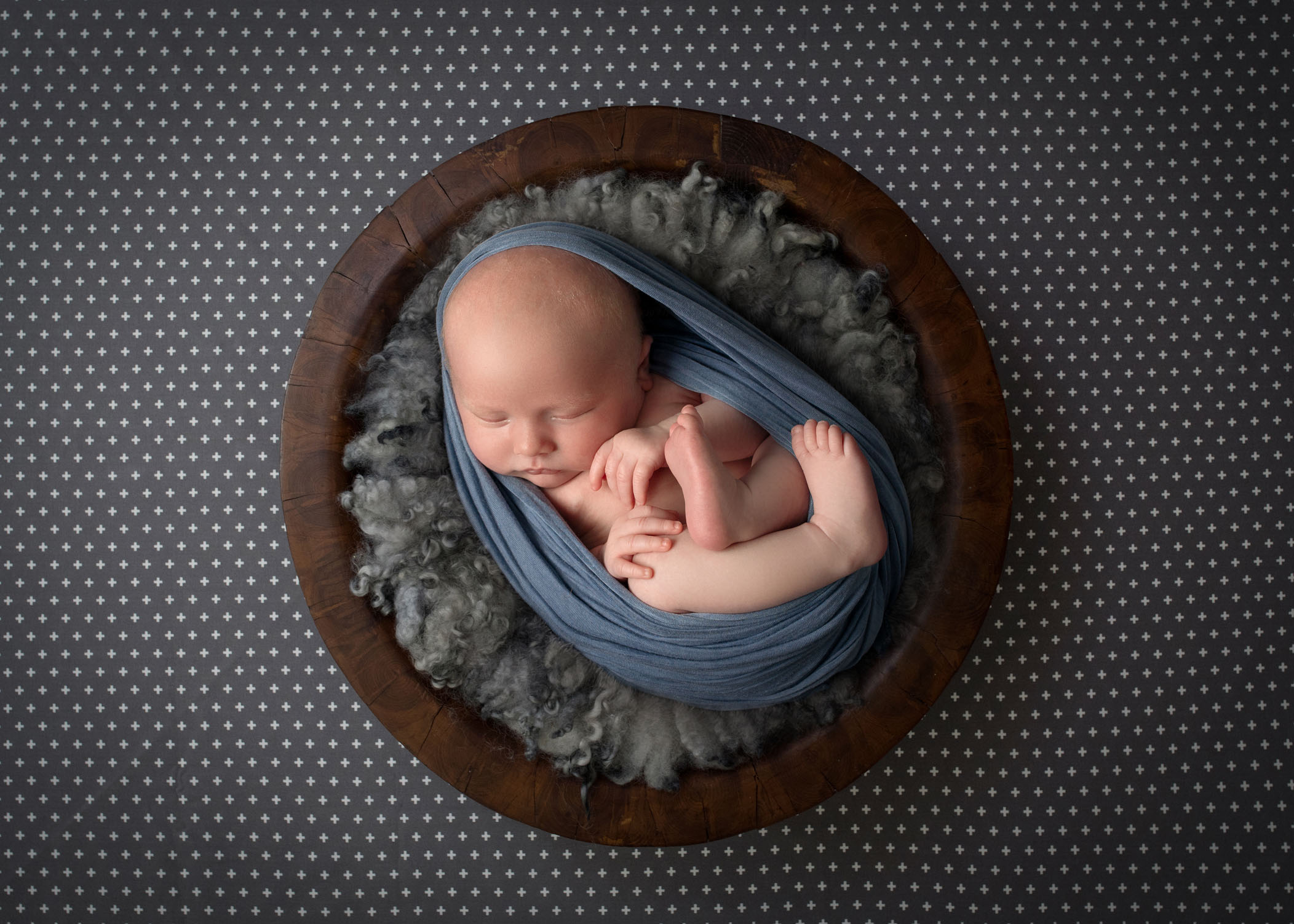 sleeping newborn wrapped in egg wrap inside wooden bowl filled with soft grey fluff