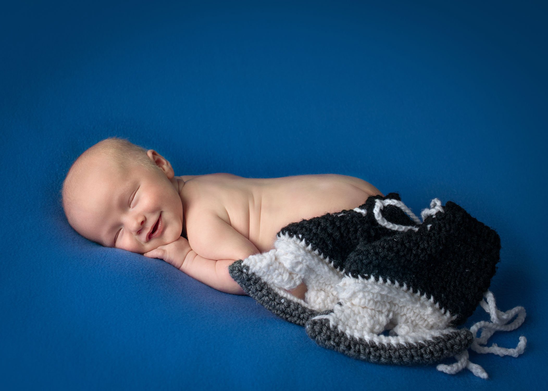 smiling newborn boy sleeping with knitted ice skates resting against him