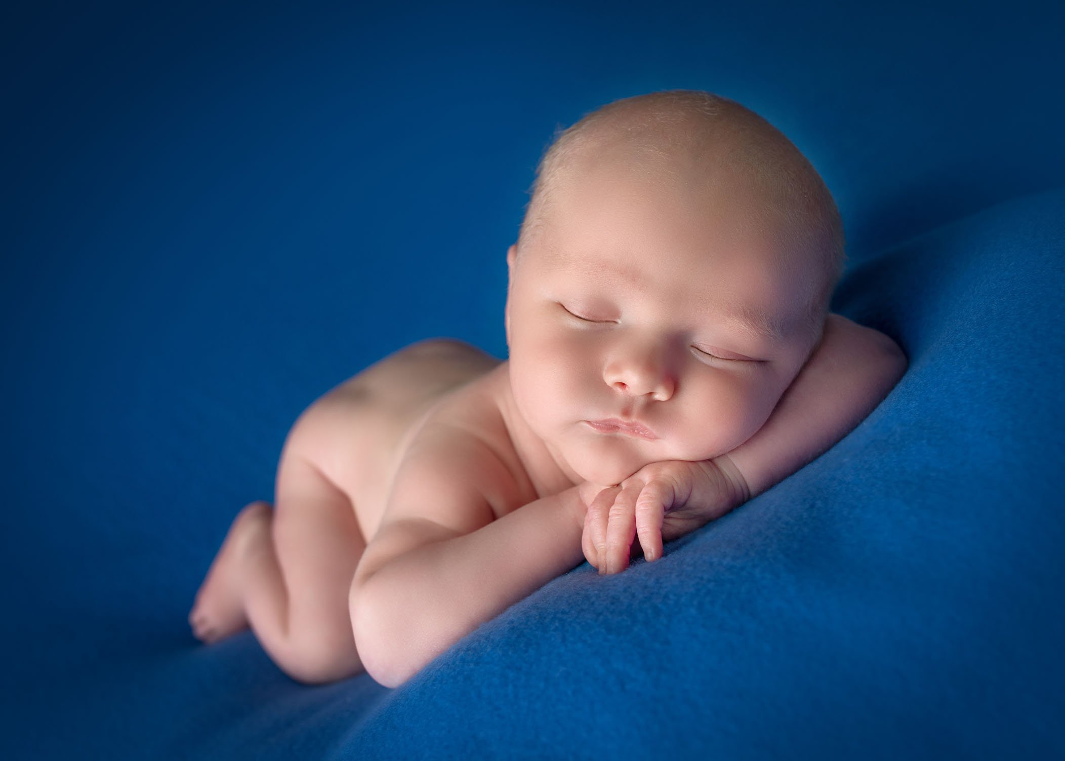 newborn boy sleeping on his tummy with head resting on his arms on blue background