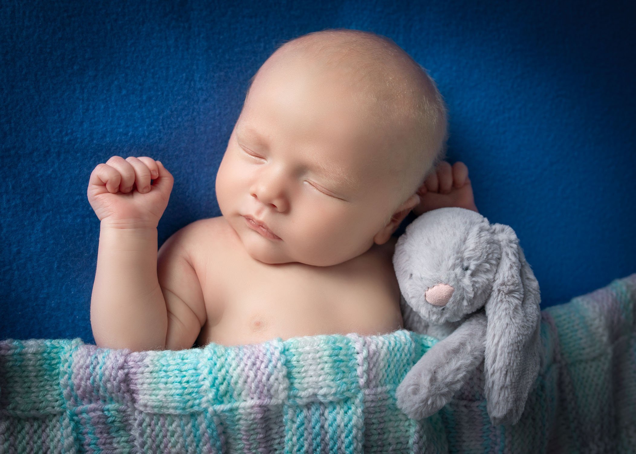 newborn baby boy sleeping under knitted blanket with stuffed rabbit