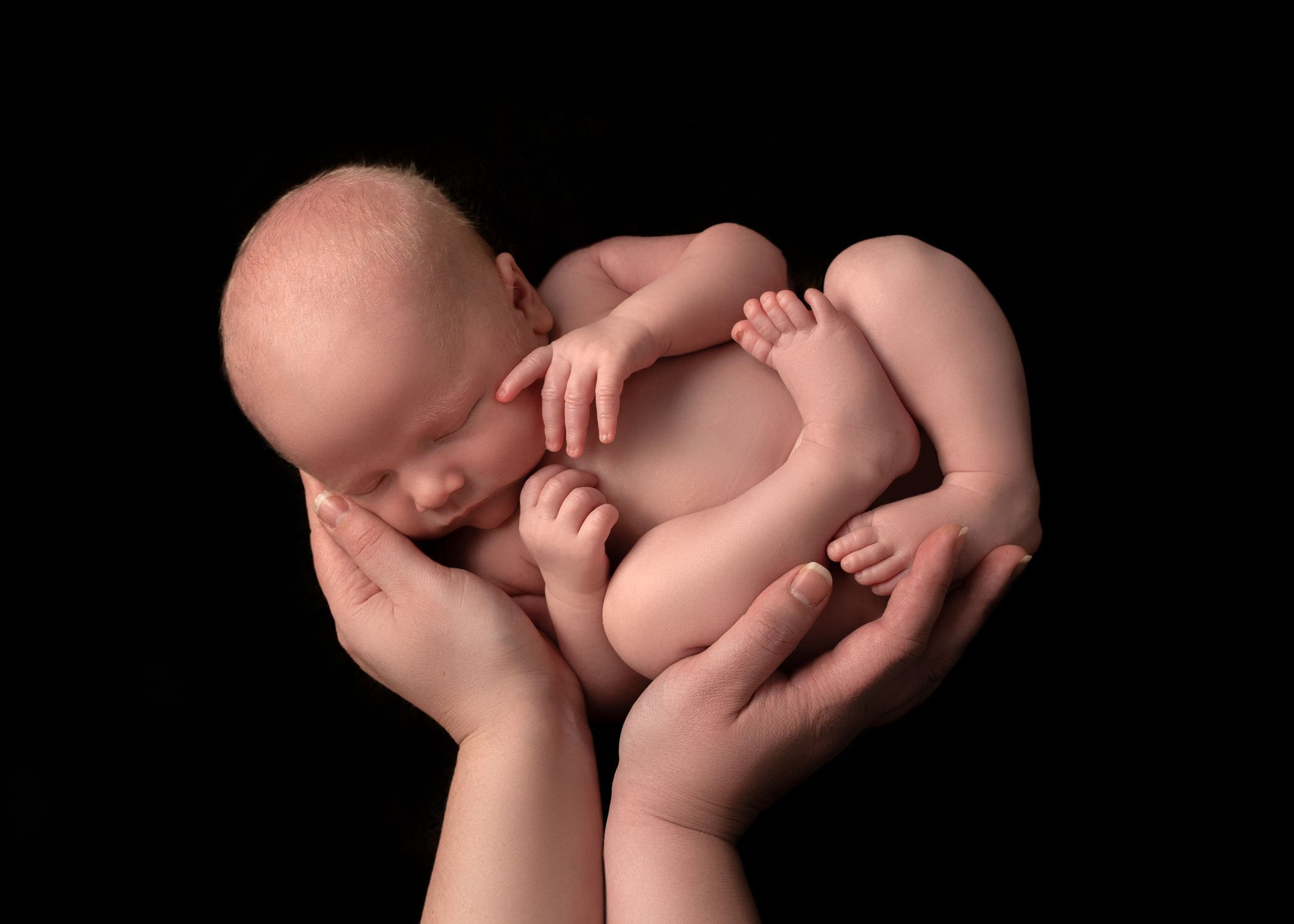 newborn boy sleeping in his mom's hands on black background