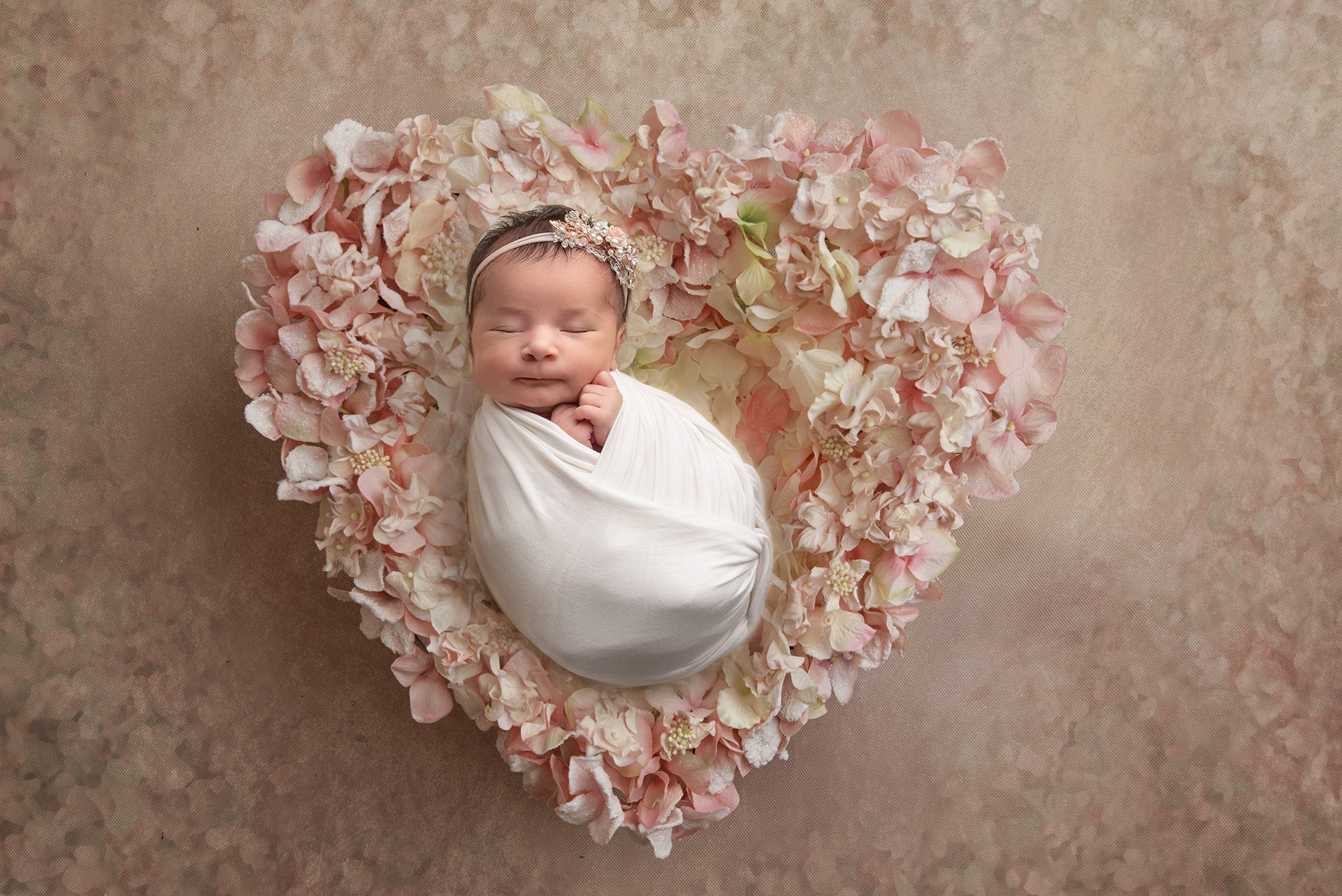 baby girl swaddled in white laying on a heart of pink florals sound asleep