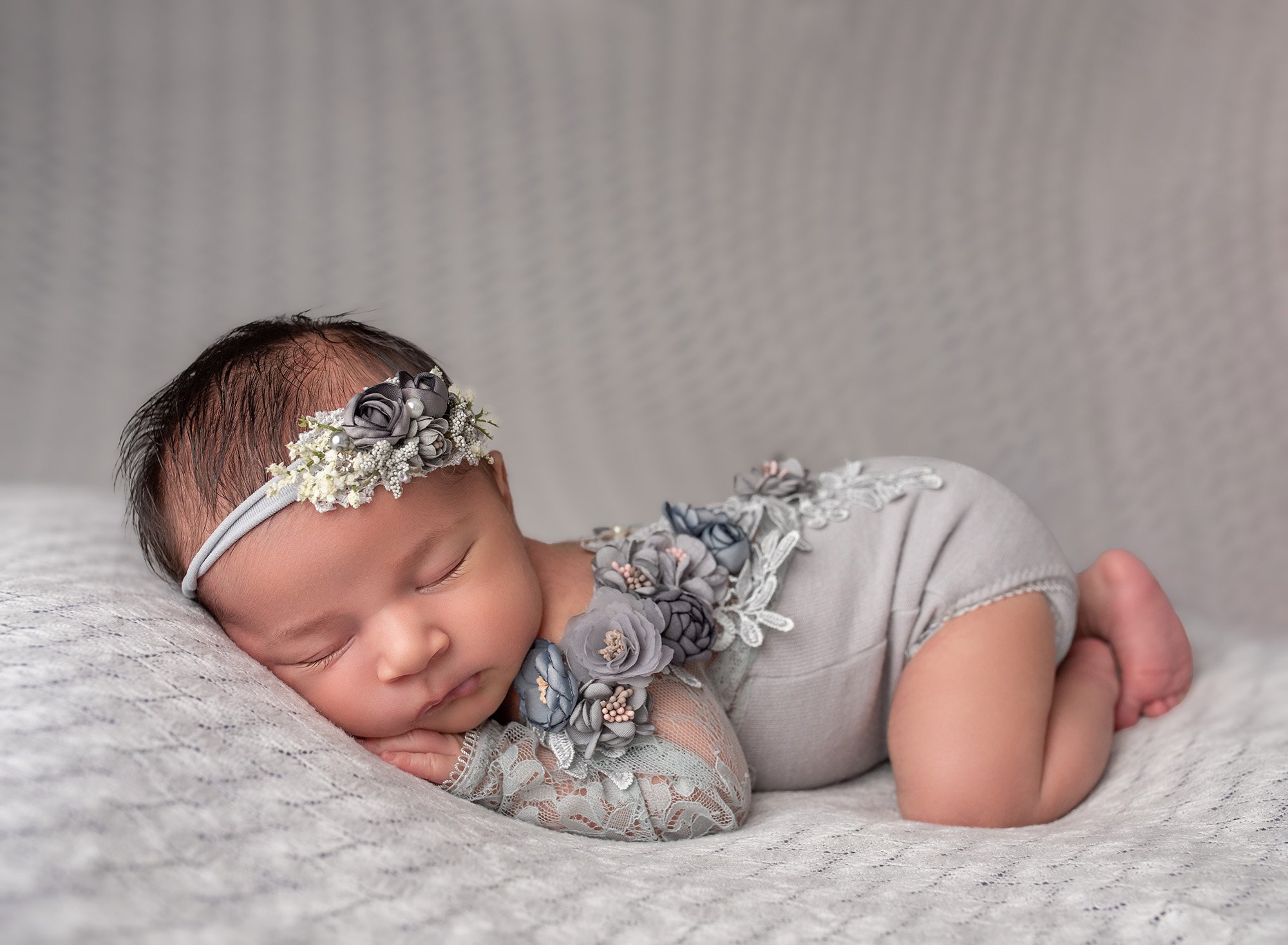 newborn baby girl laying on stomach dressed in a floral gray body suit with gray floral headband