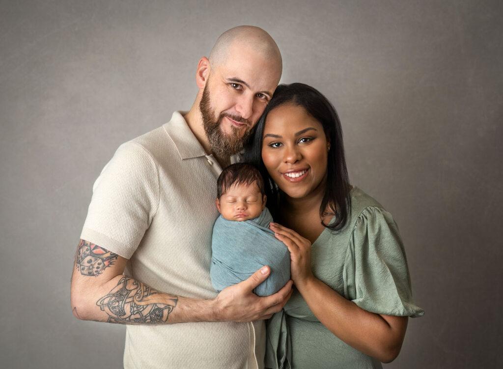 Parents holding swaddled newborn together for family portrait in studio
