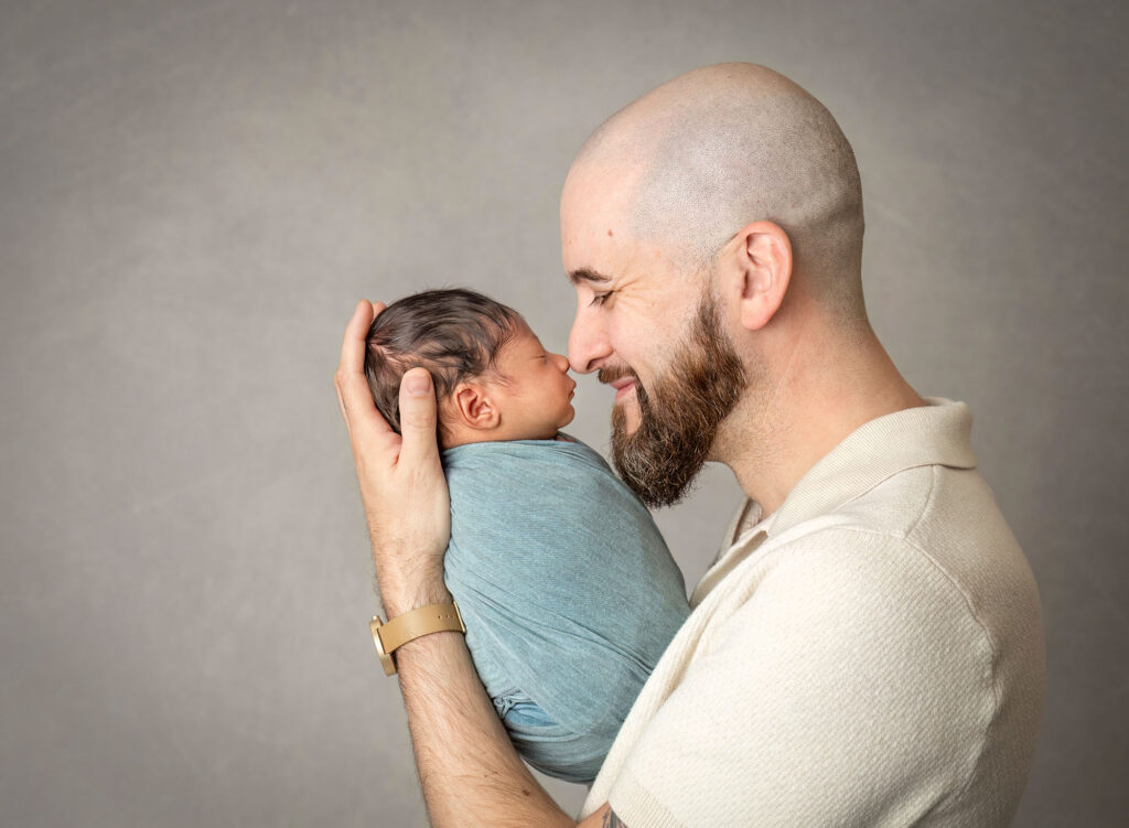 Father touching noses with swaddled baby in an awake newborn photo session