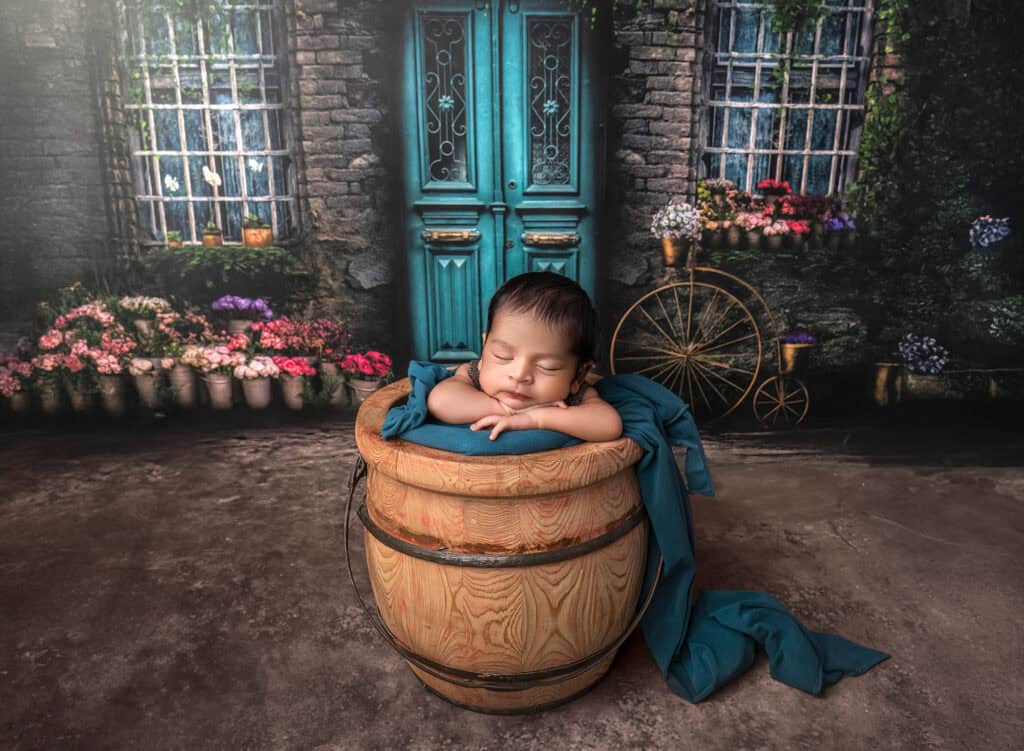newborn and family photography with baby in wooden barrel set and teal wrap in floral courtyard