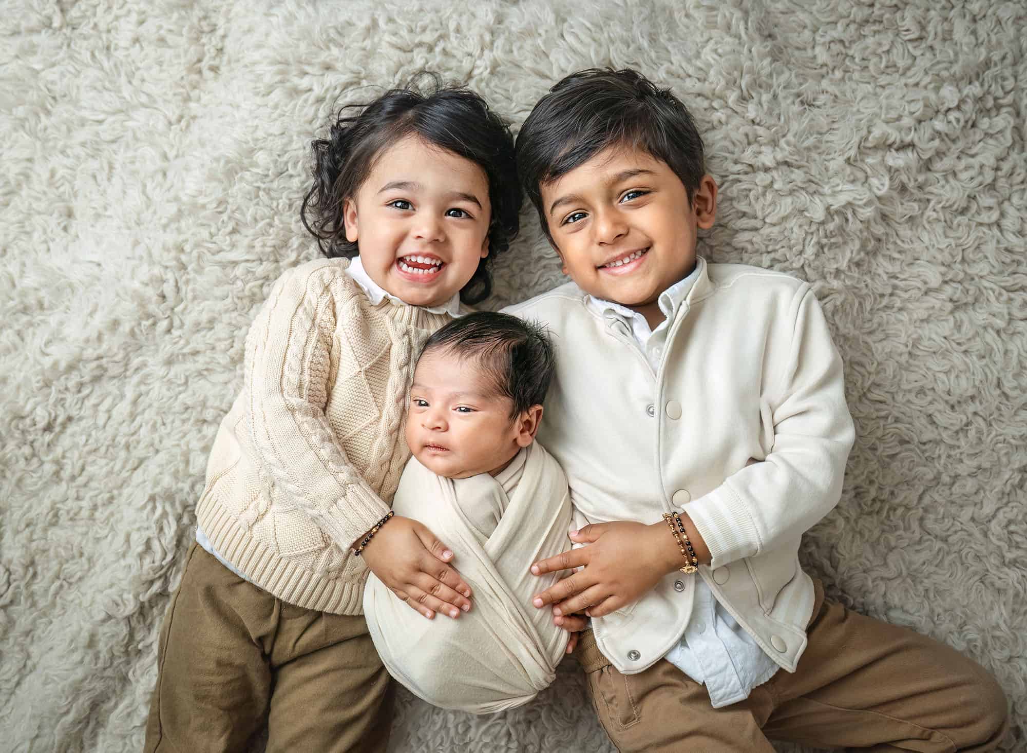 newborn and family photography of brothers cuddling baby on ivory flokati