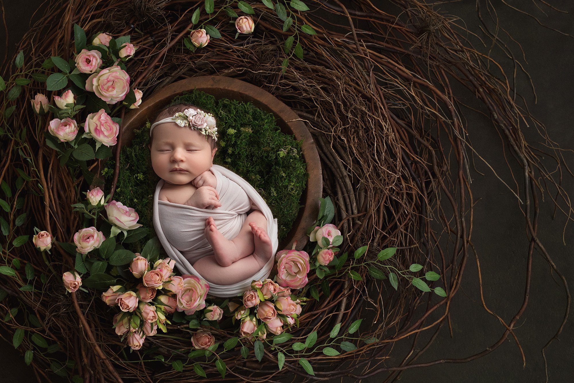 swaddled baby girl wearing floral headband laying on moss and pink and white roses