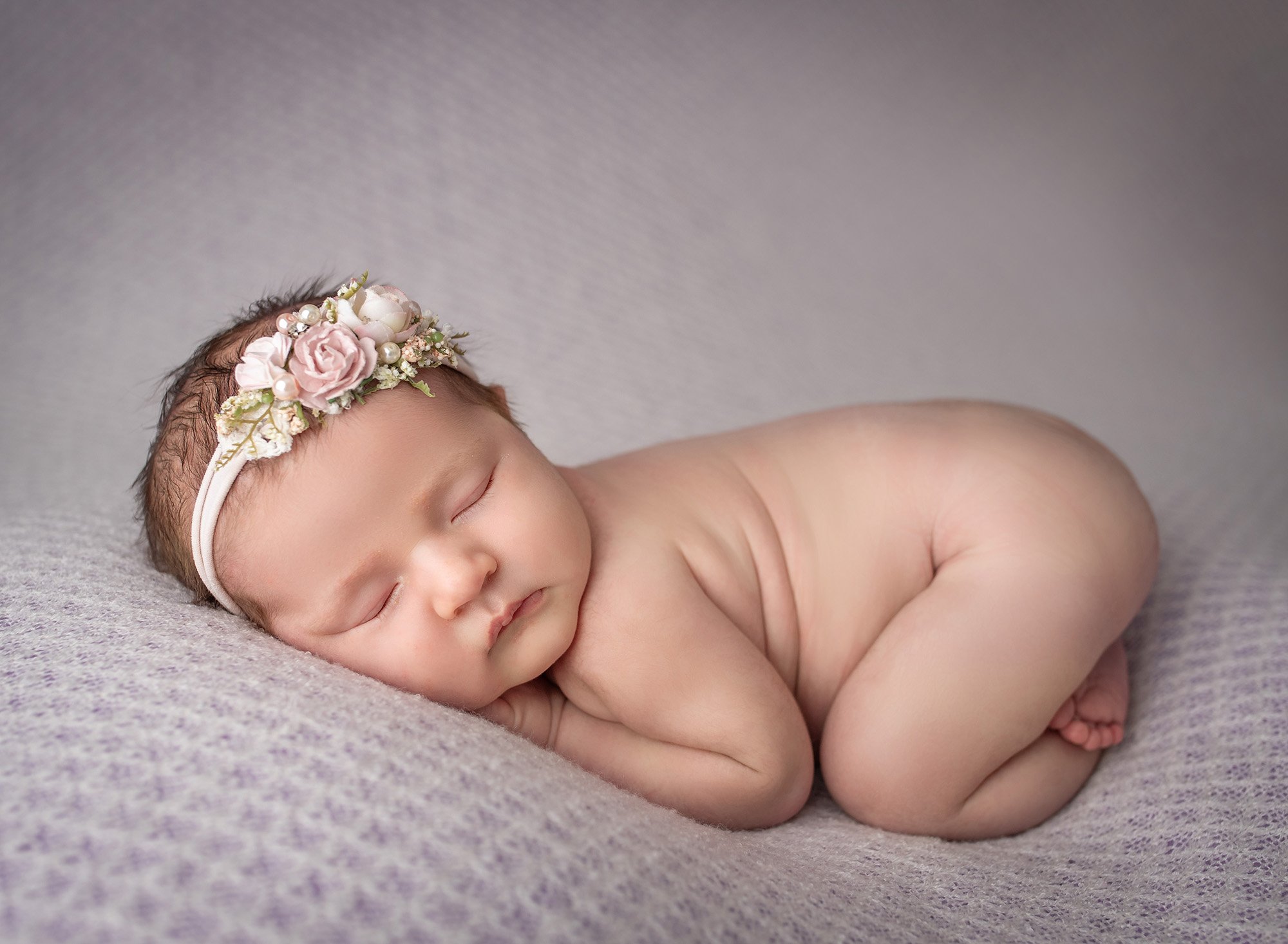 naked baby girl laying on her stomach with elegant floral headband on white blanket