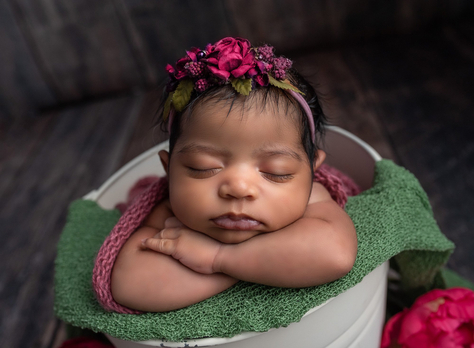 newborn baby girl wearing deep pink floral headband asleep in a bucket