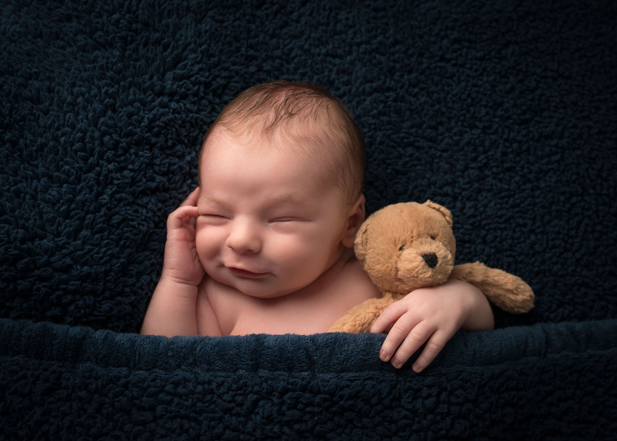 newborn boy smiling and sleeping with teddy bear