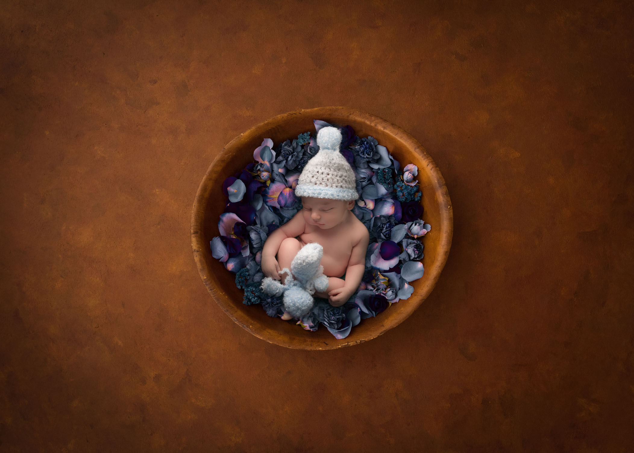 newborn boy wearing knitted cap and booties in bowl of flower petals