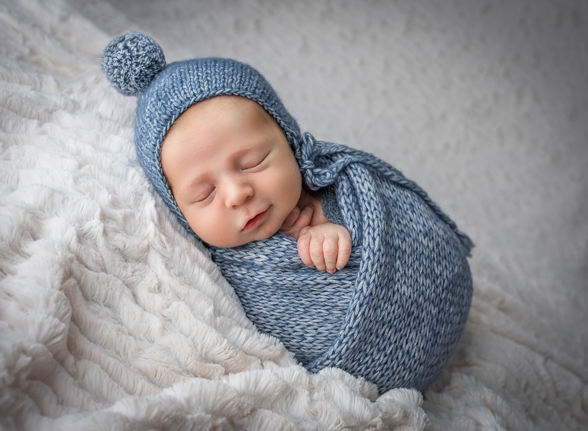 newborn baby boy swaddled in blue fast asleep on a fluffy blanket