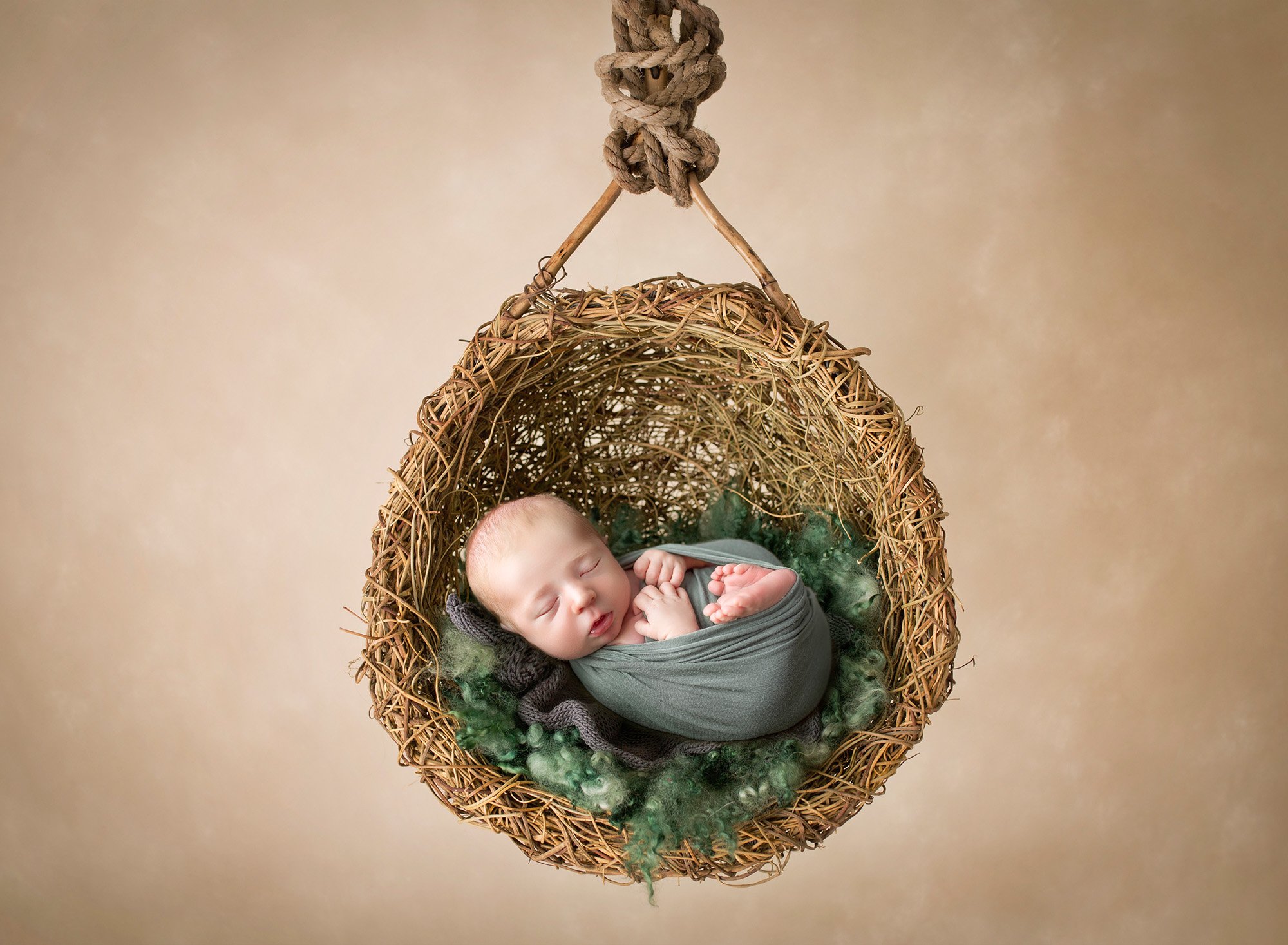 newborn baby boy swaddled in green fast asleep in a hanging twined nest