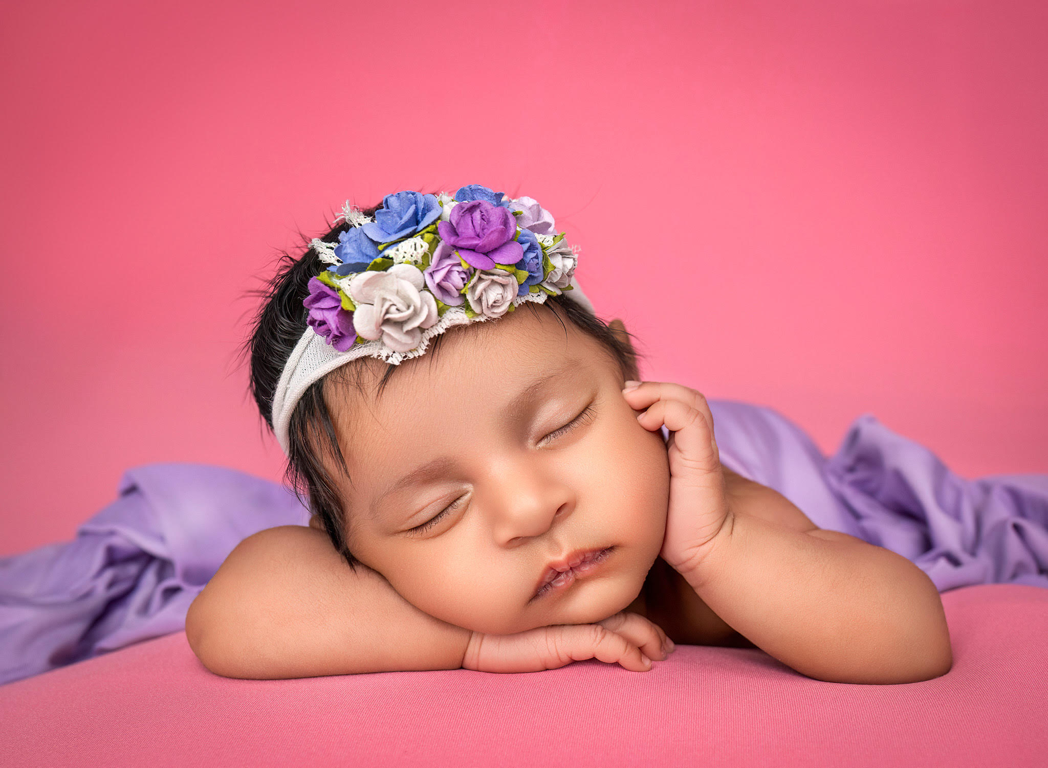 Newborn baby girl wearing purple resting head on hands 