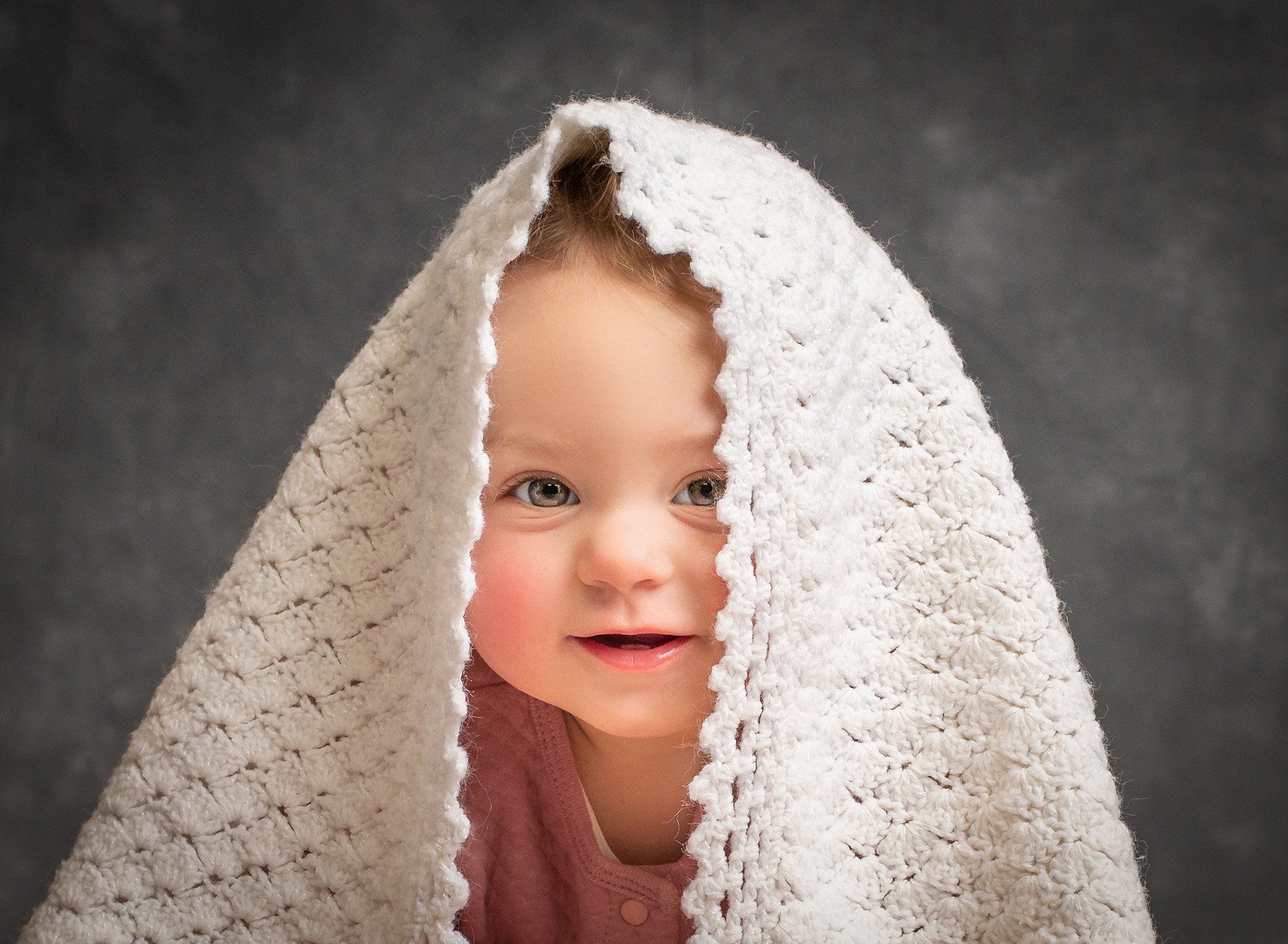 smiling baby girl in pink with white blanket covering her