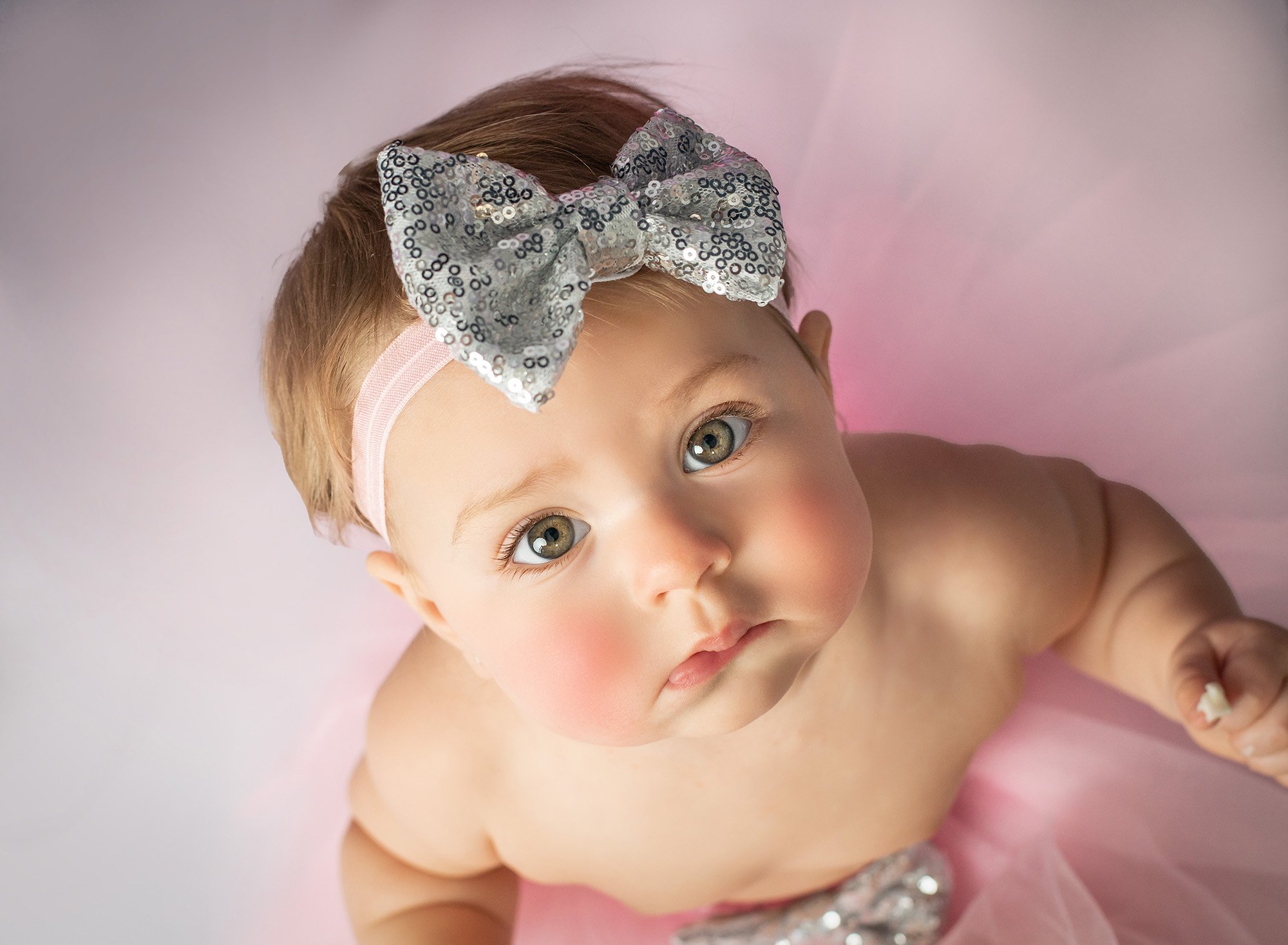 one year old baby girl with hazel eyes wearing a silver sequined bow