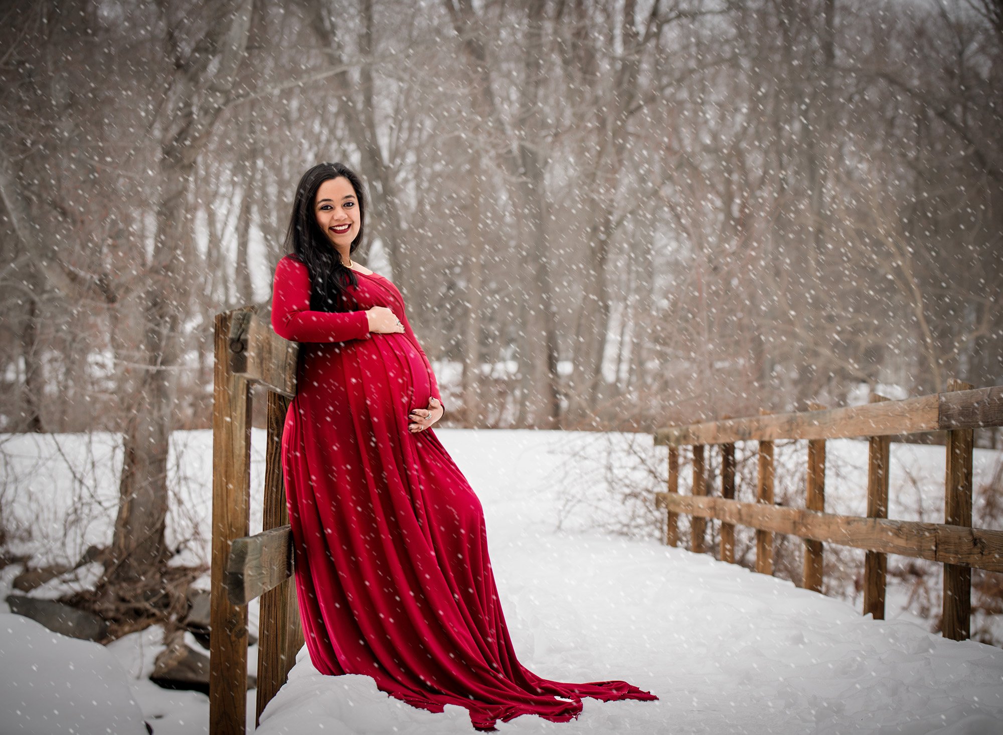 red maternity gown on snowy bridge with snow falling