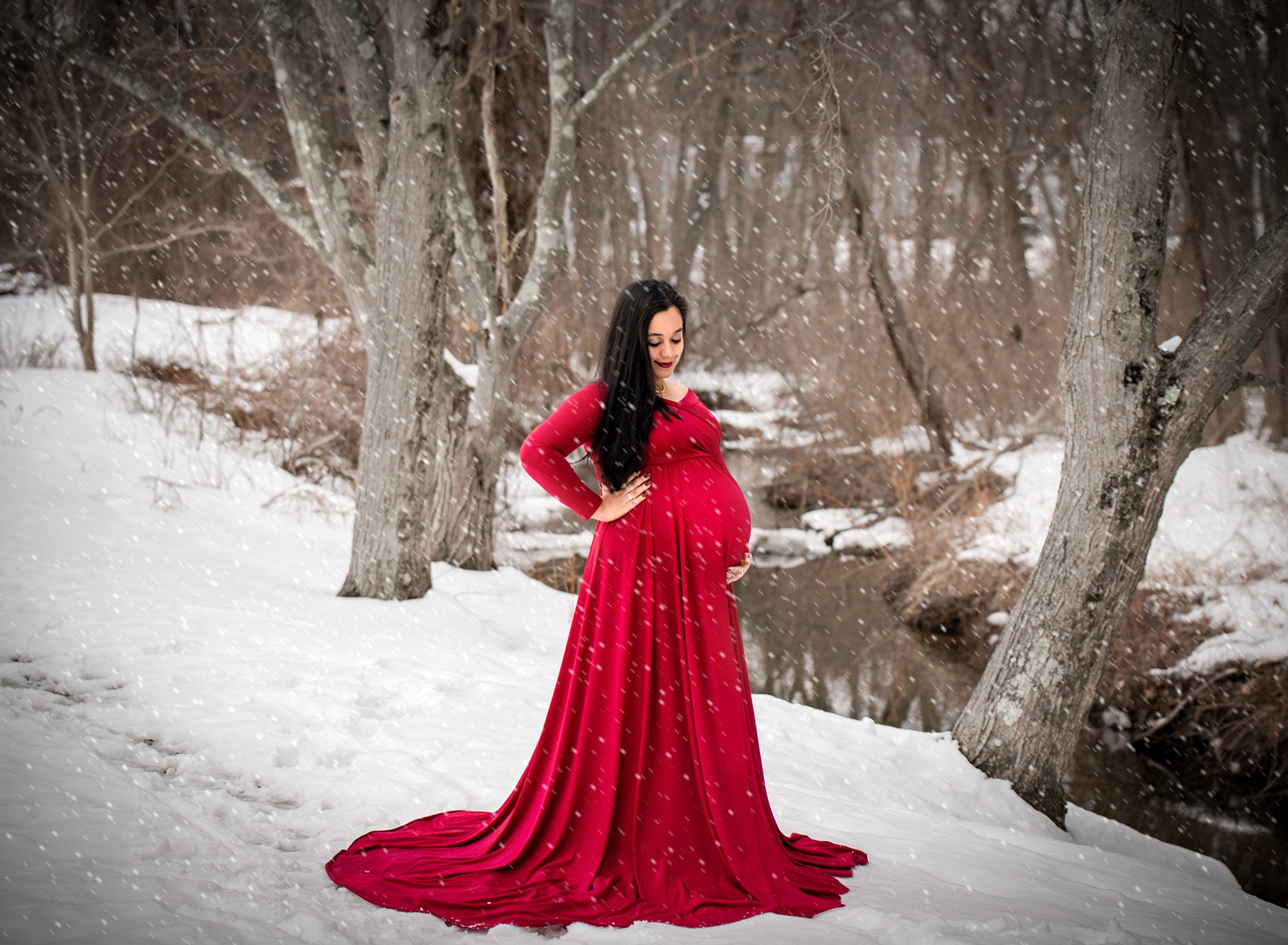 red maternity gown by the stream with snowflakes falling around her