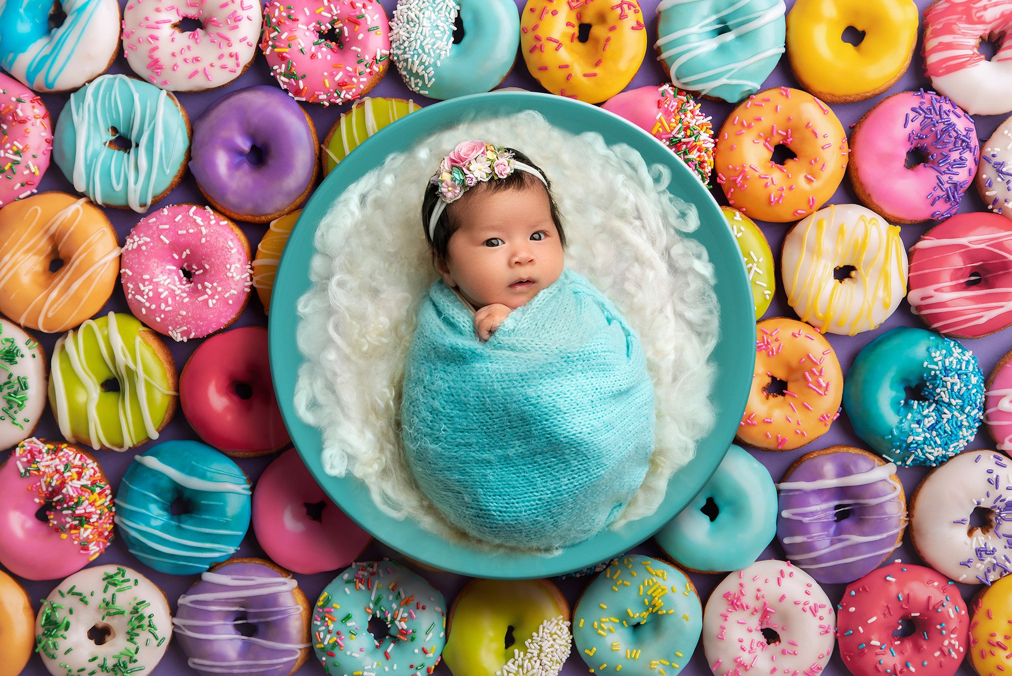 vibrant newborn photo awake newborn baby girl swaddled in an aqua sweater wrap laying in aqua bowl with fuzzy white blanket on a donut background
