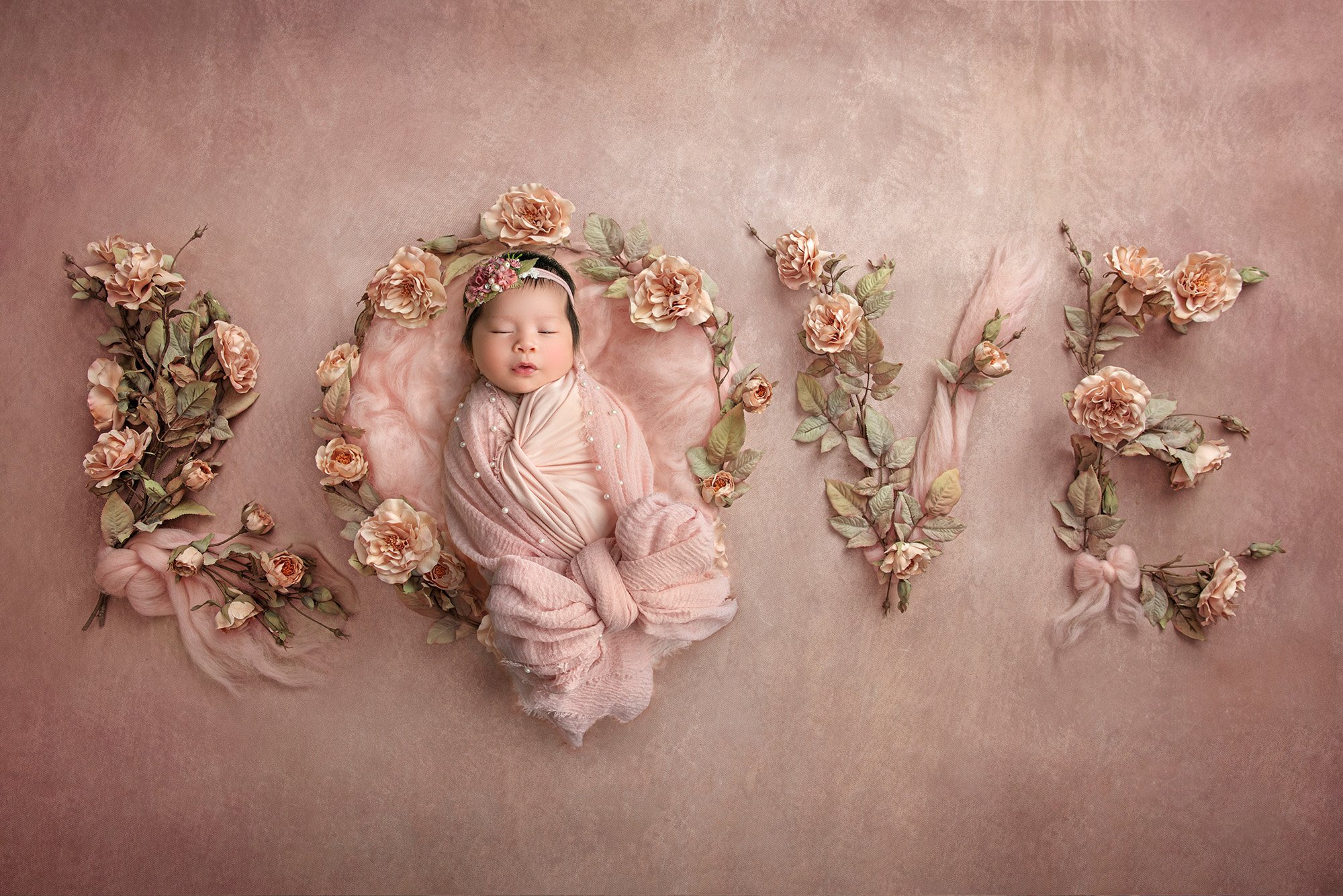 sweet newborn baby girl asleep on a pink background spelling out the word LOVE in flowers and bows