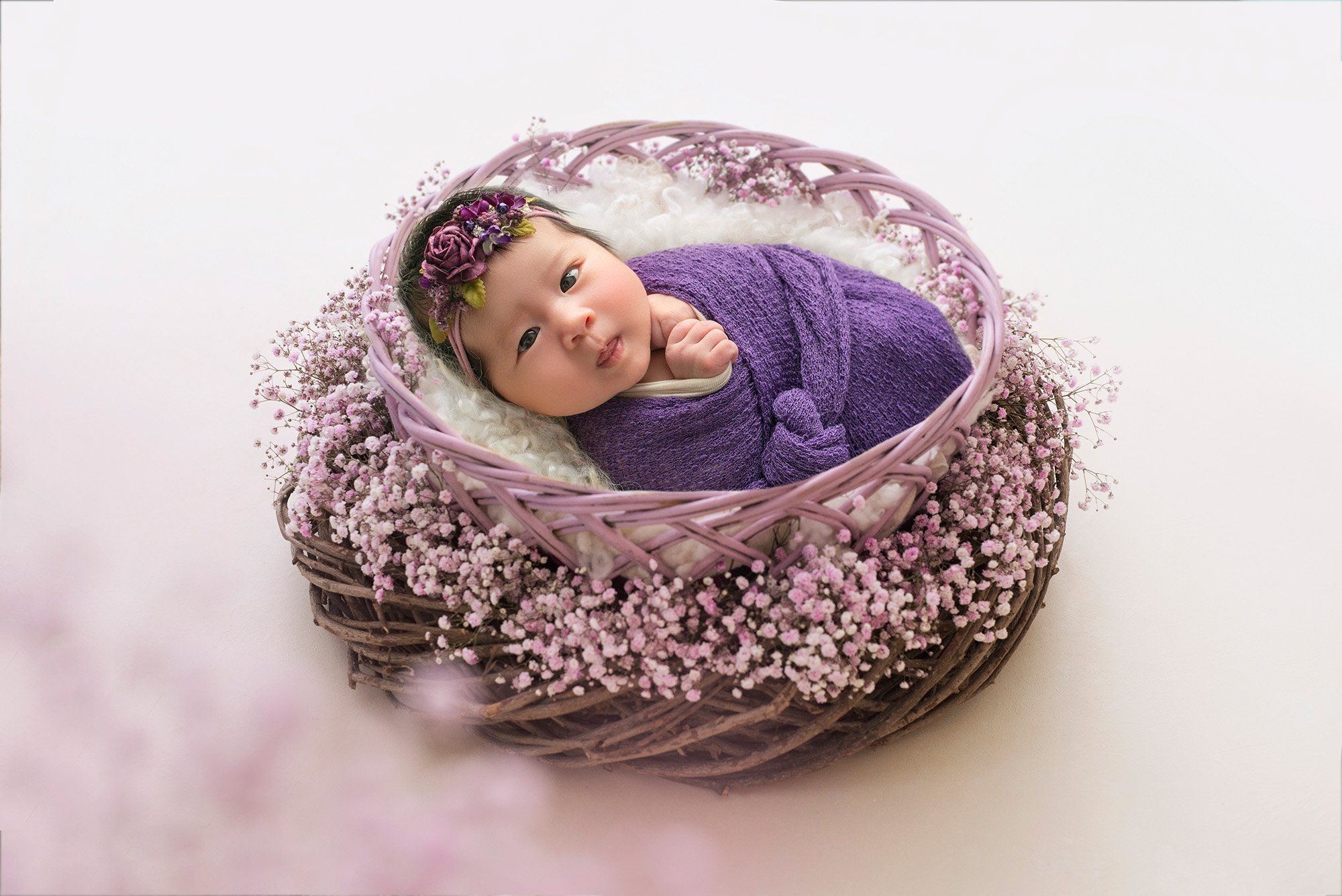 best time to do newborn photos month old baby girl swaddled in purple wrap in a lavender nest looking at the camera with eyes open best time to take newborn photos