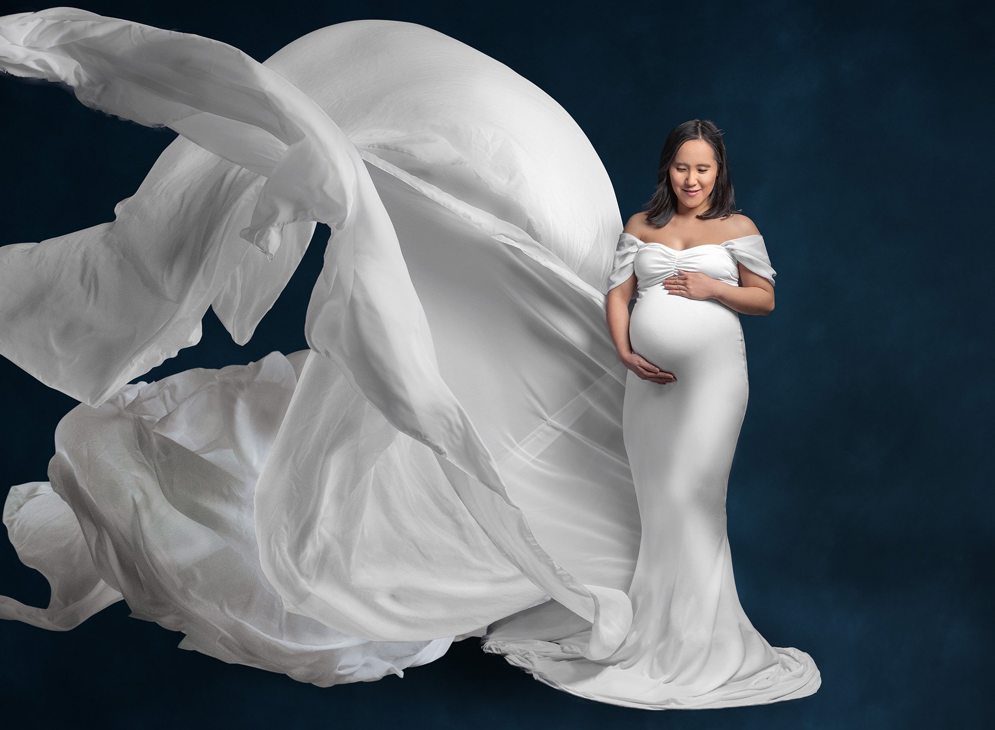 vibrant maternity photo brunette woman wearing white flowing maternity dress on a navy blue background