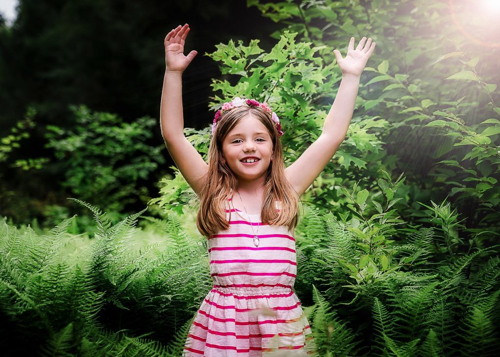 little girl with her hands in the air outside in summer with the sun shining on her