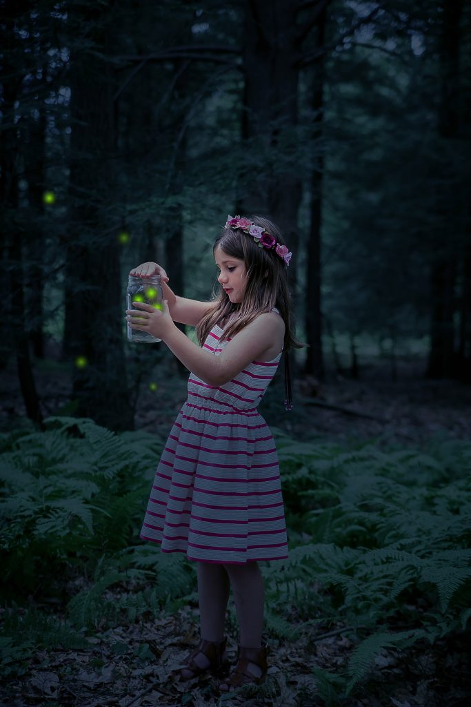 little girl outside at night with green lightening bugs in a jar
