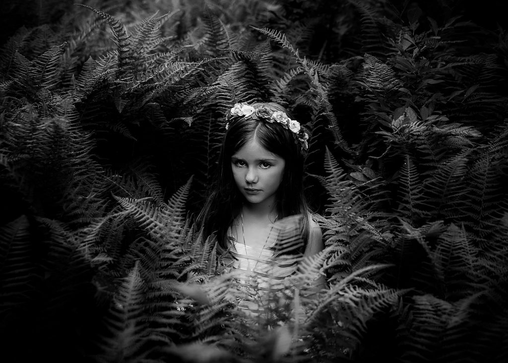 dramatic black and white image of little girl sitting in ferns