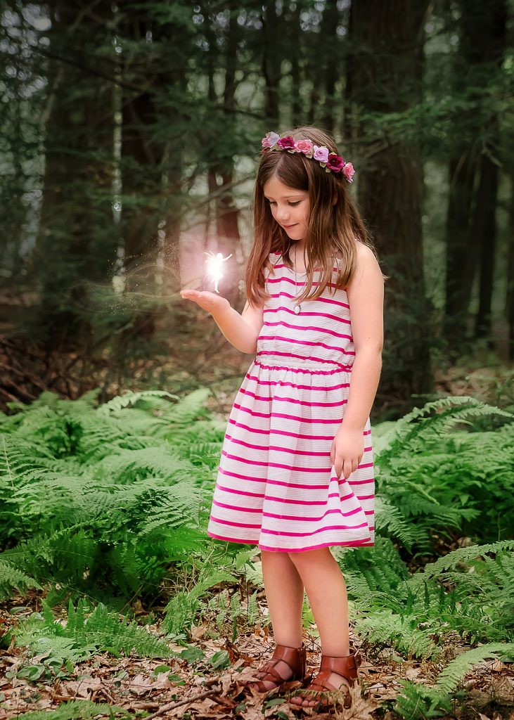 little girl outside in the woods with a pink glowing fairy in her hand