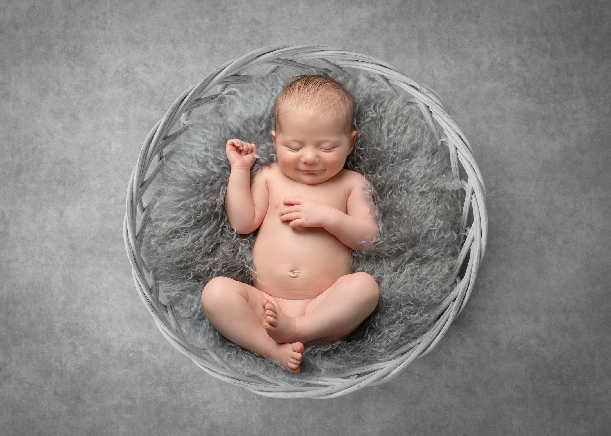 newborn sleeping in grey fur bowl smiling