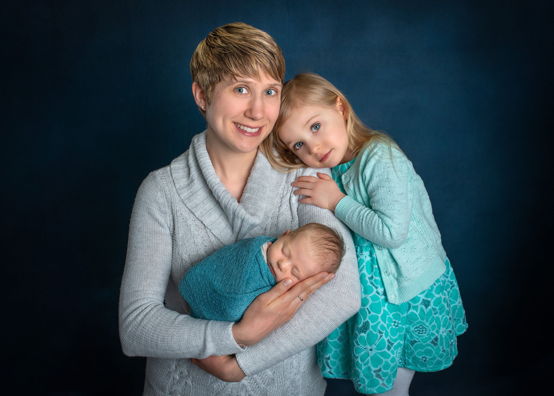 Mom holding newborn with toddler girl hugging her arm