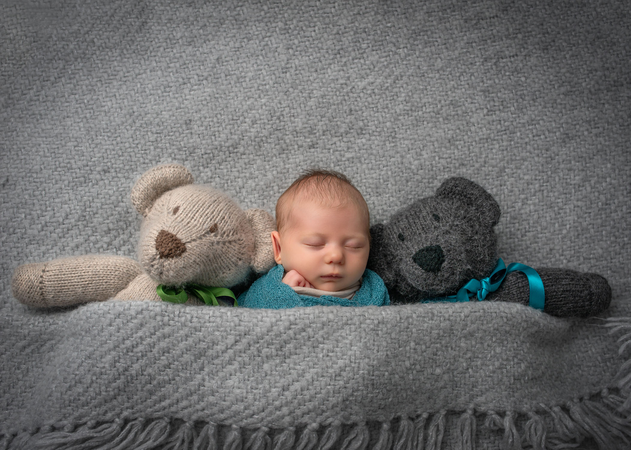 baby girl sleeping tucked in blanket with two stuffed teddy bears