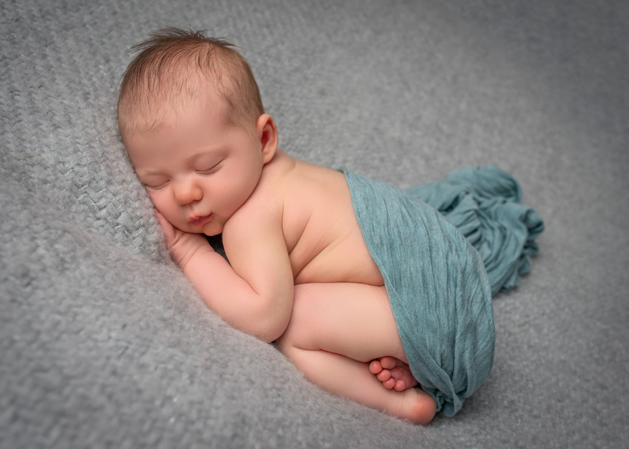 baby girl sleeping on her tummy on grey blanket with teal wrap over her bottom