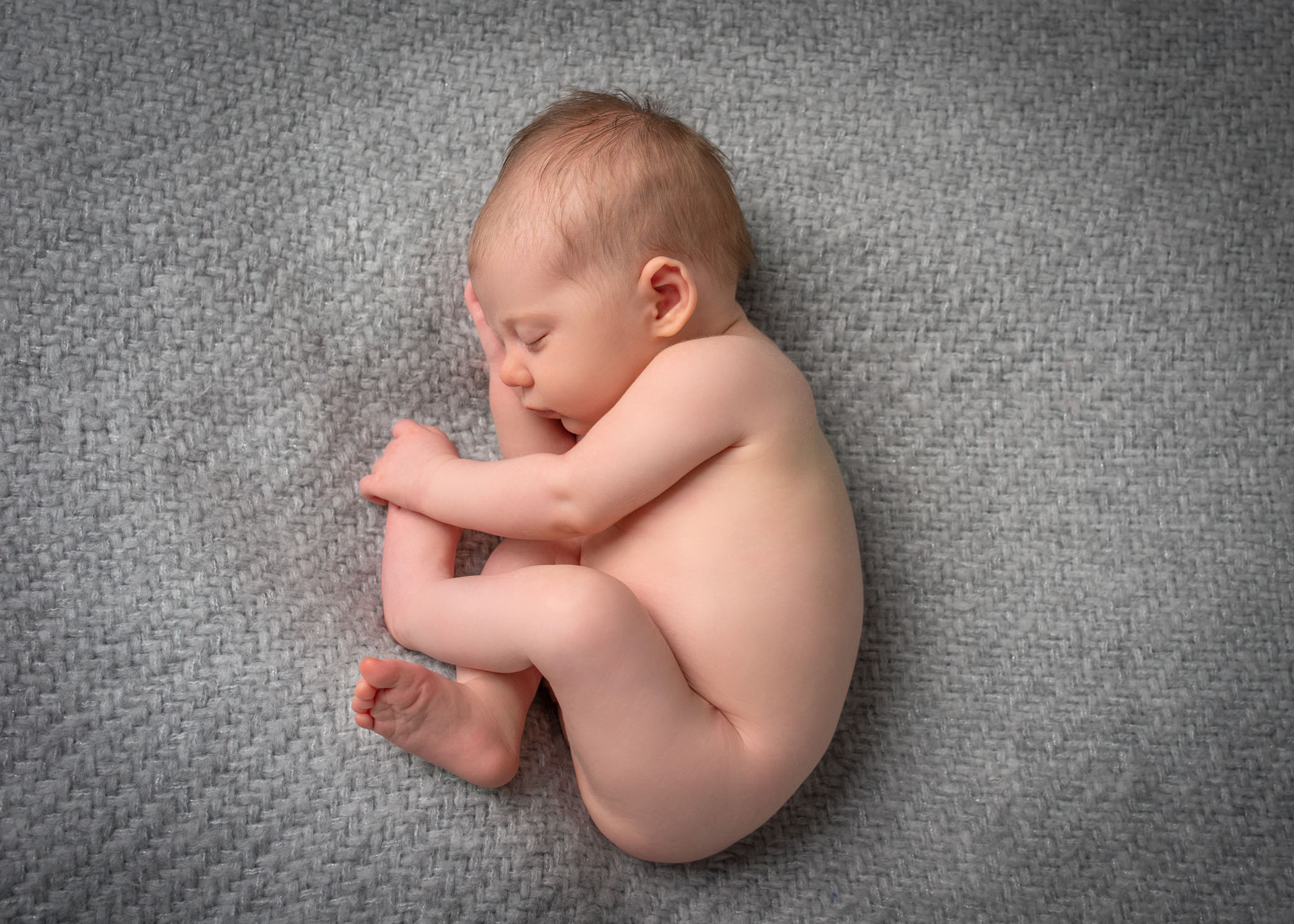 newborn baby girl sleeping on grey blanket on her side in womb like pose